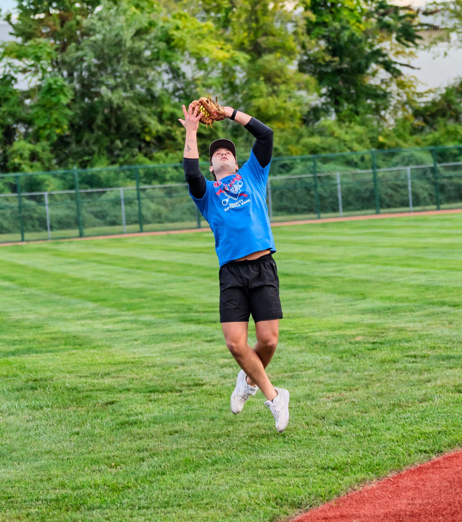 Male outfielder in blue jersey leaping to catch fly ball with glove raised above head on grass.