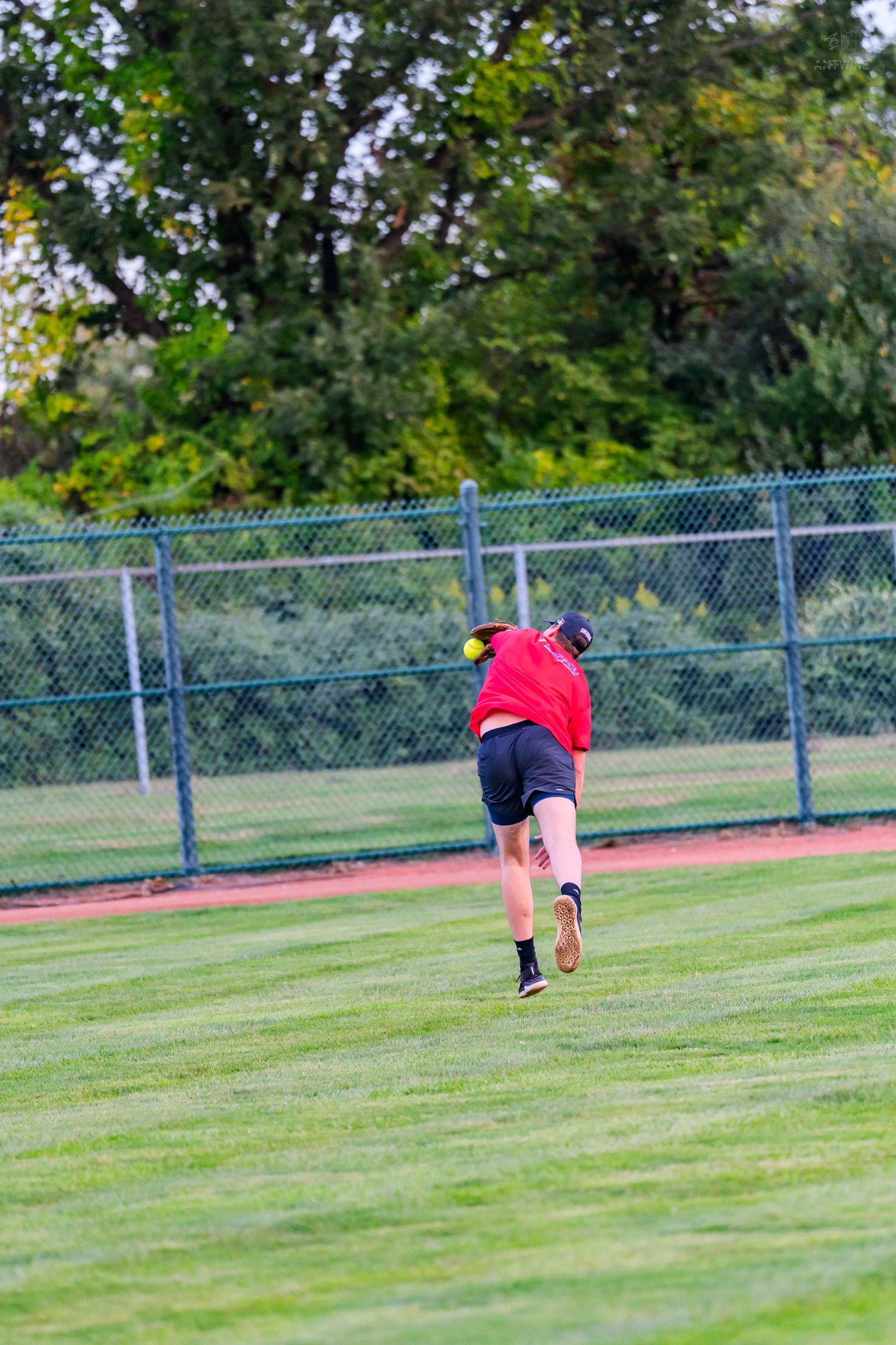 A baseball outfielder in a red shirt and black shorts runs across a green grass field during a game.