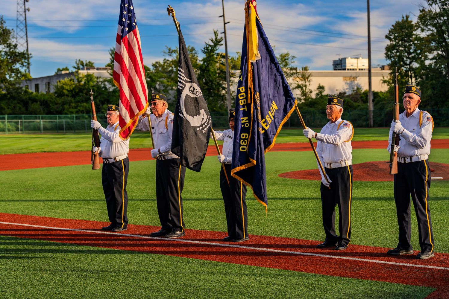Color guard presenting American and military flags on a baseball field during a ceremonial event.