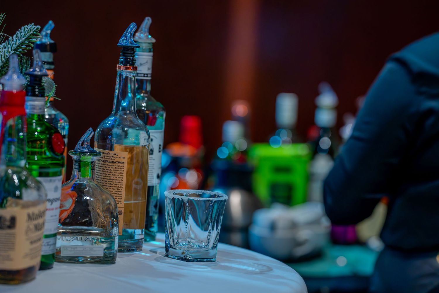 Assorted liquor bottles and crystal glasses displayed on a white table at a bar event.