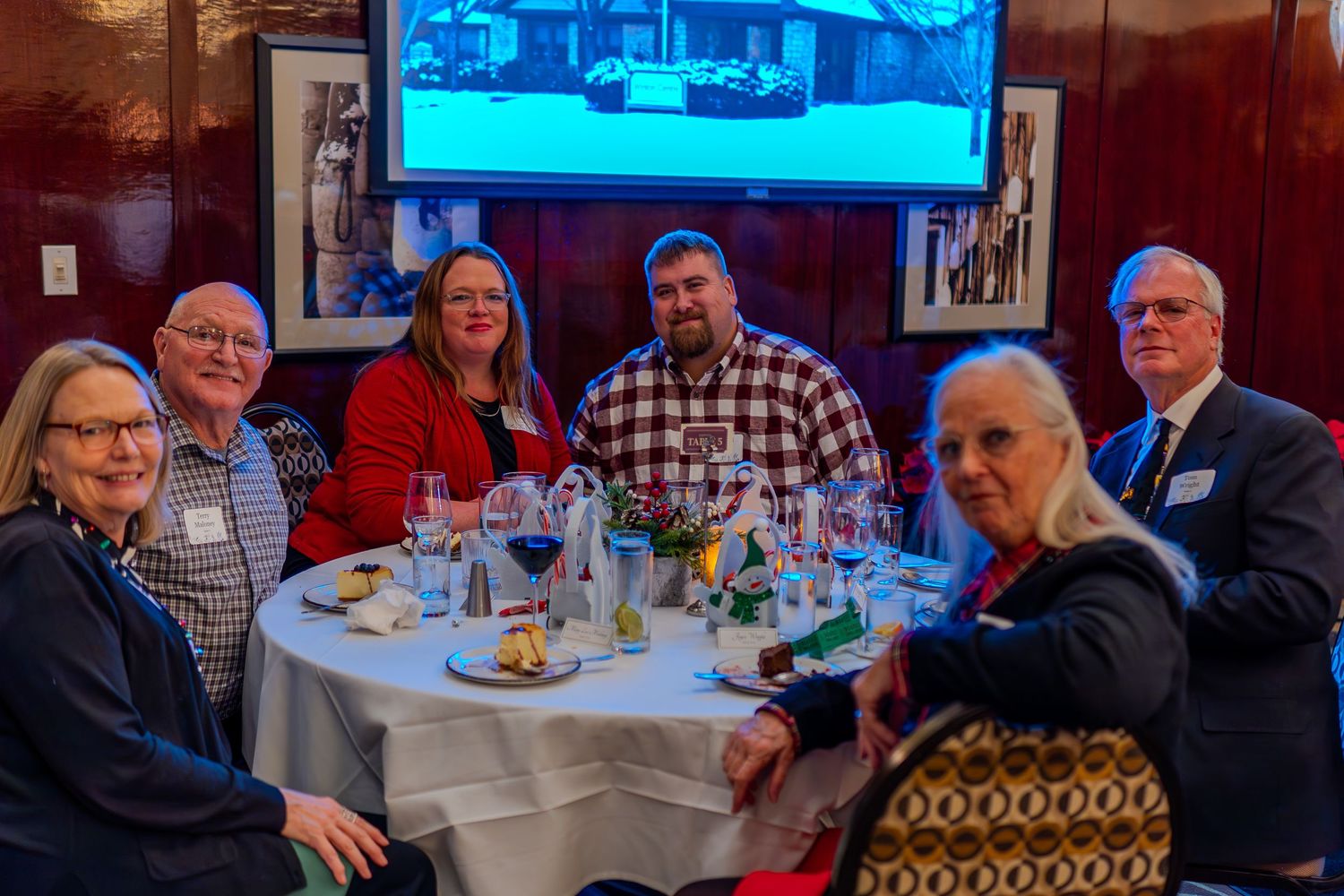 Six people smile around a elegantly set dining table at a formal restaurant gathering or reunion event.