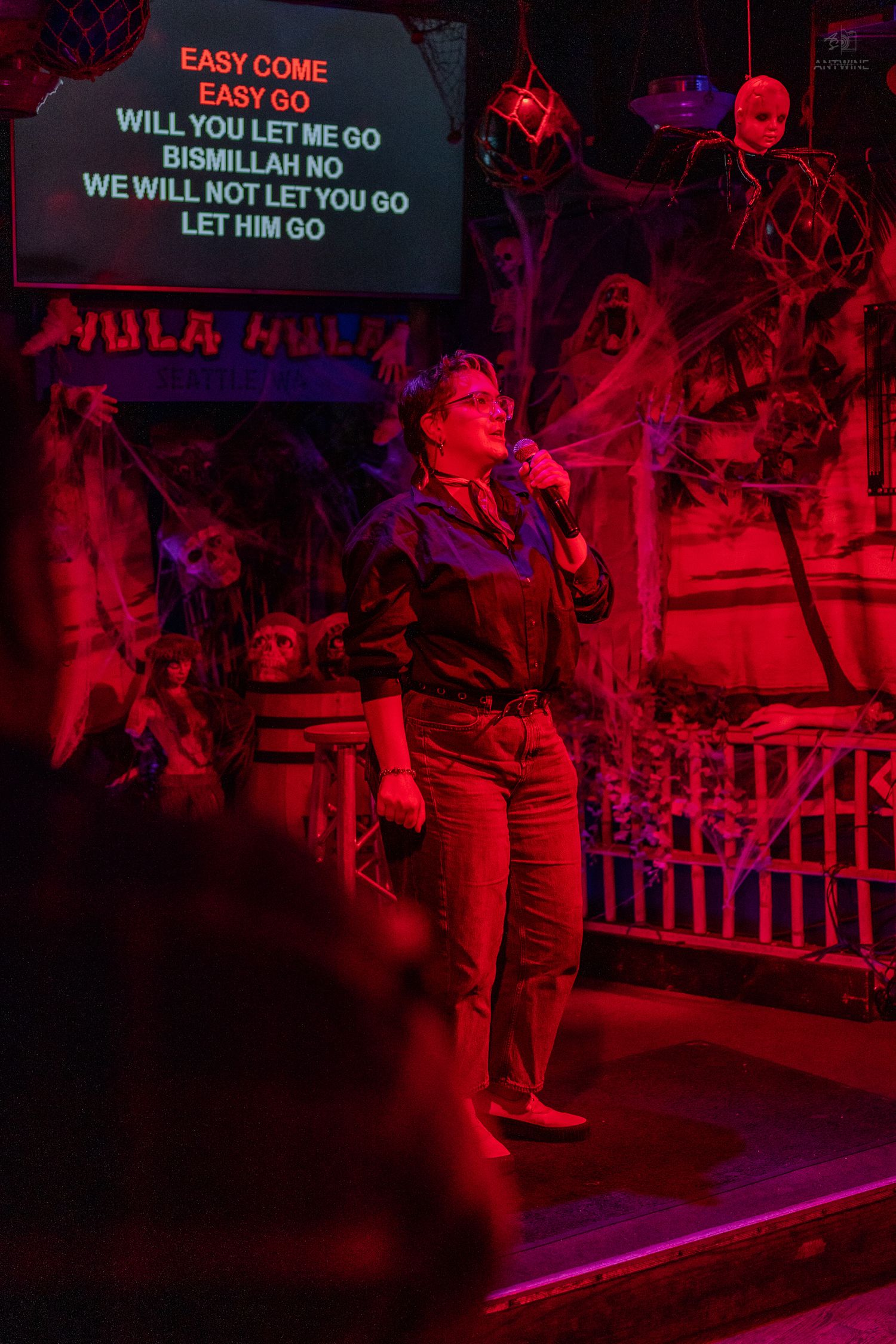 Woman singing karaoke to Bohemian Rhapsody under red lights in a Halloween-decorated bar in Seattle.