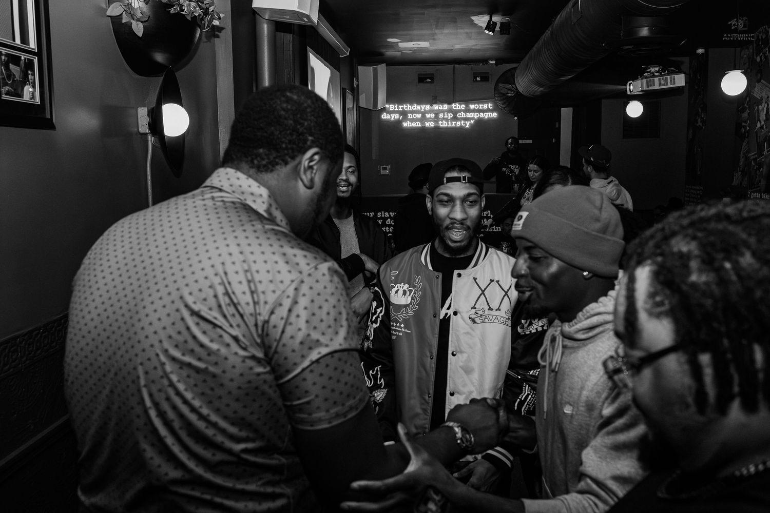 Black and white photo of young men socializing and networking at an indoor music or social event.