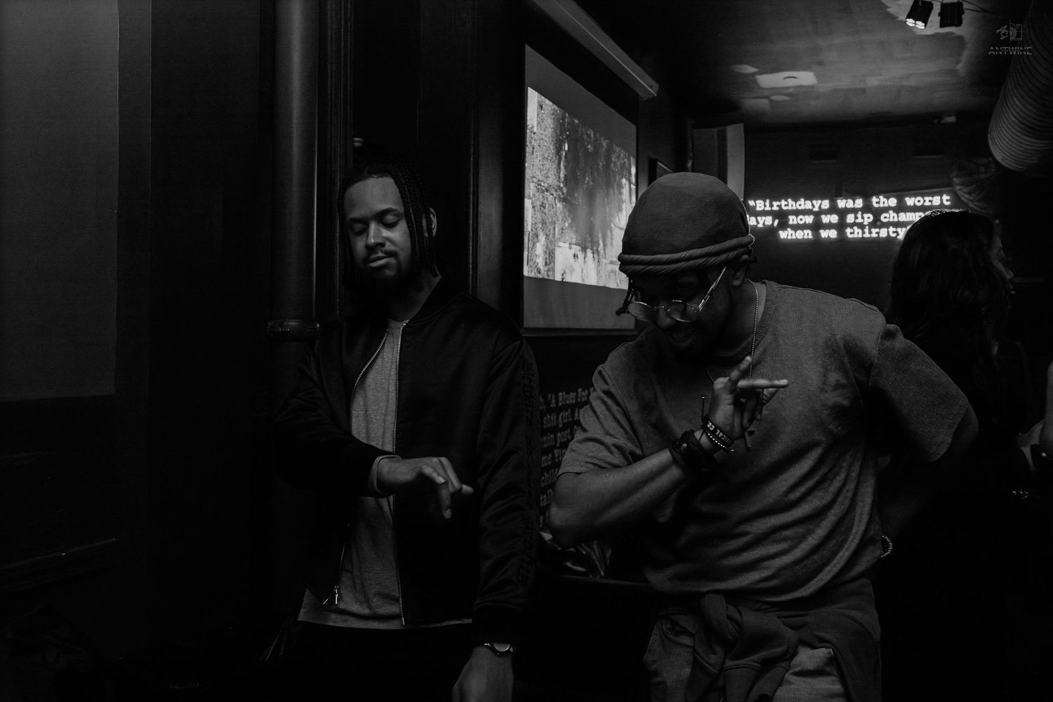 Two men standing in a dimly lit room with a projection screen in a black and white photo.