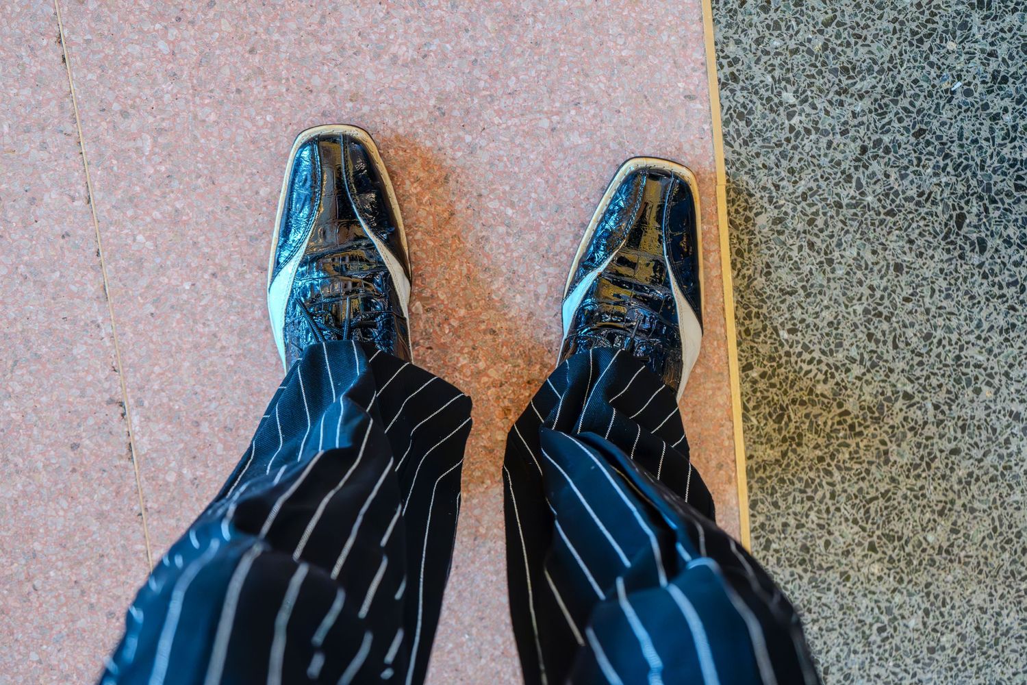 Person wearing black pinstripe pants and shiny blue embroidered shoes standing on a tiled surface.