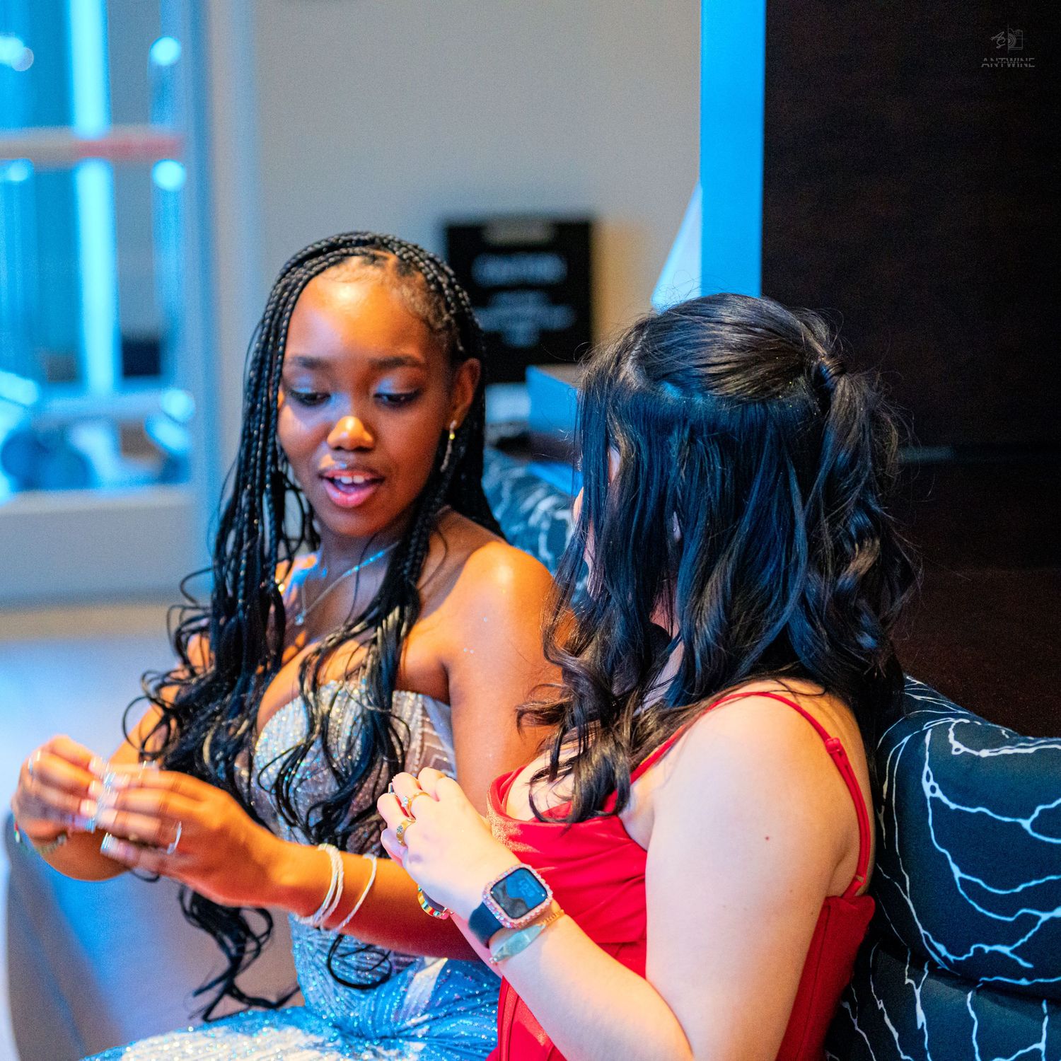 Two young women in formal dresses looking down together at a shared item in a candid moment.