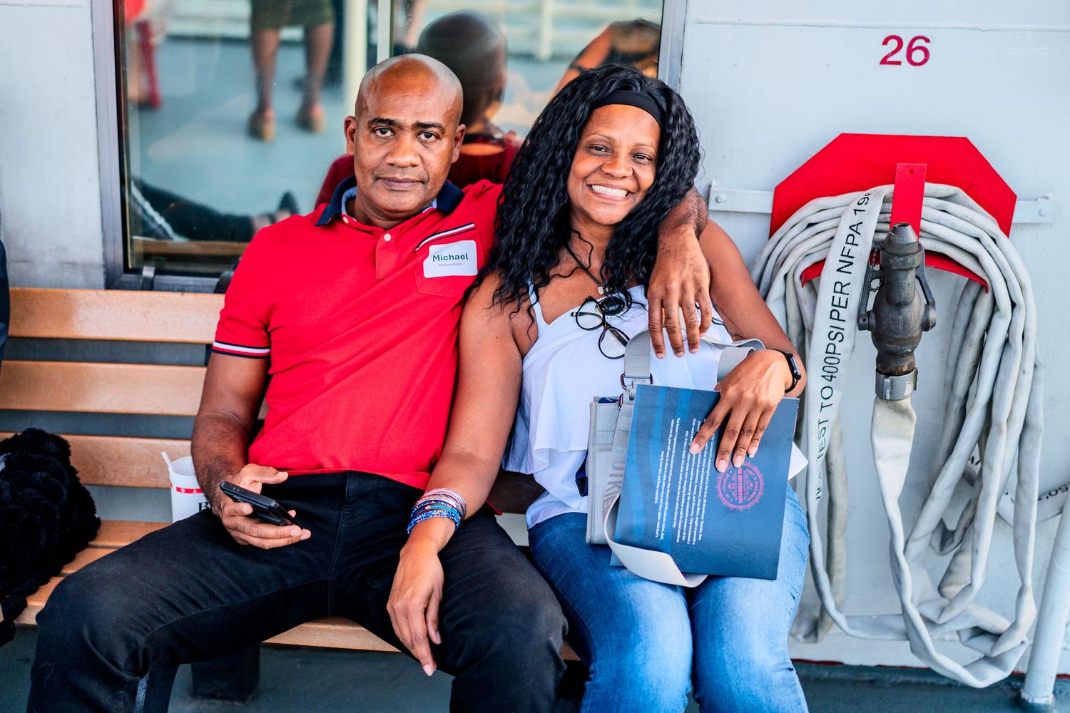 A man and woman sitting together smiling near a fire hose reel at gate 26 of a stadium.