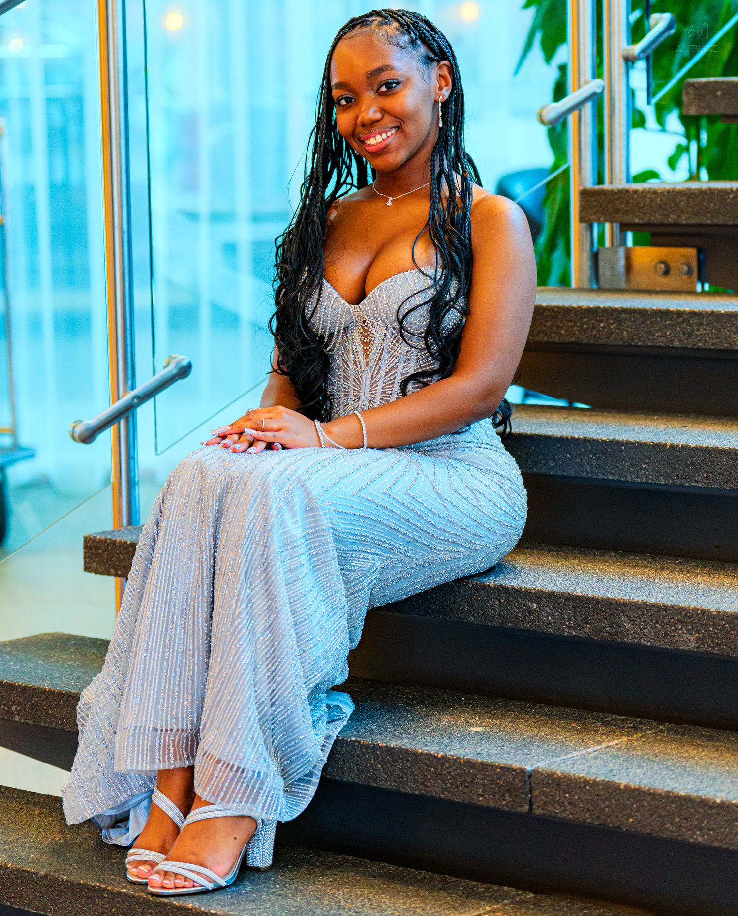 Young woman in silver striped jumpsuit with braids sitting on stairs at formal event.