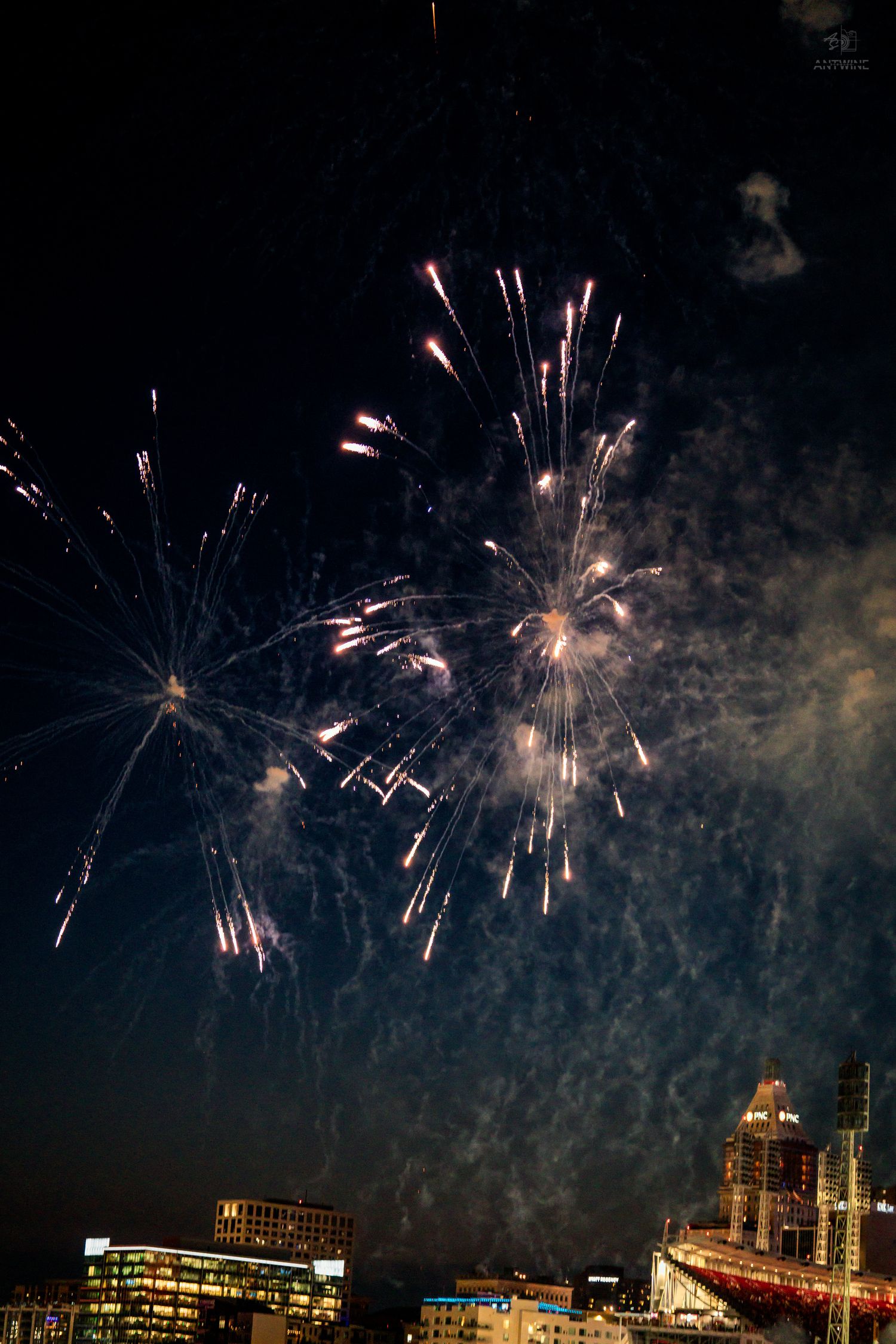 Colorful fireworks lighting up the night sky above a city skyline with buildings visible below.