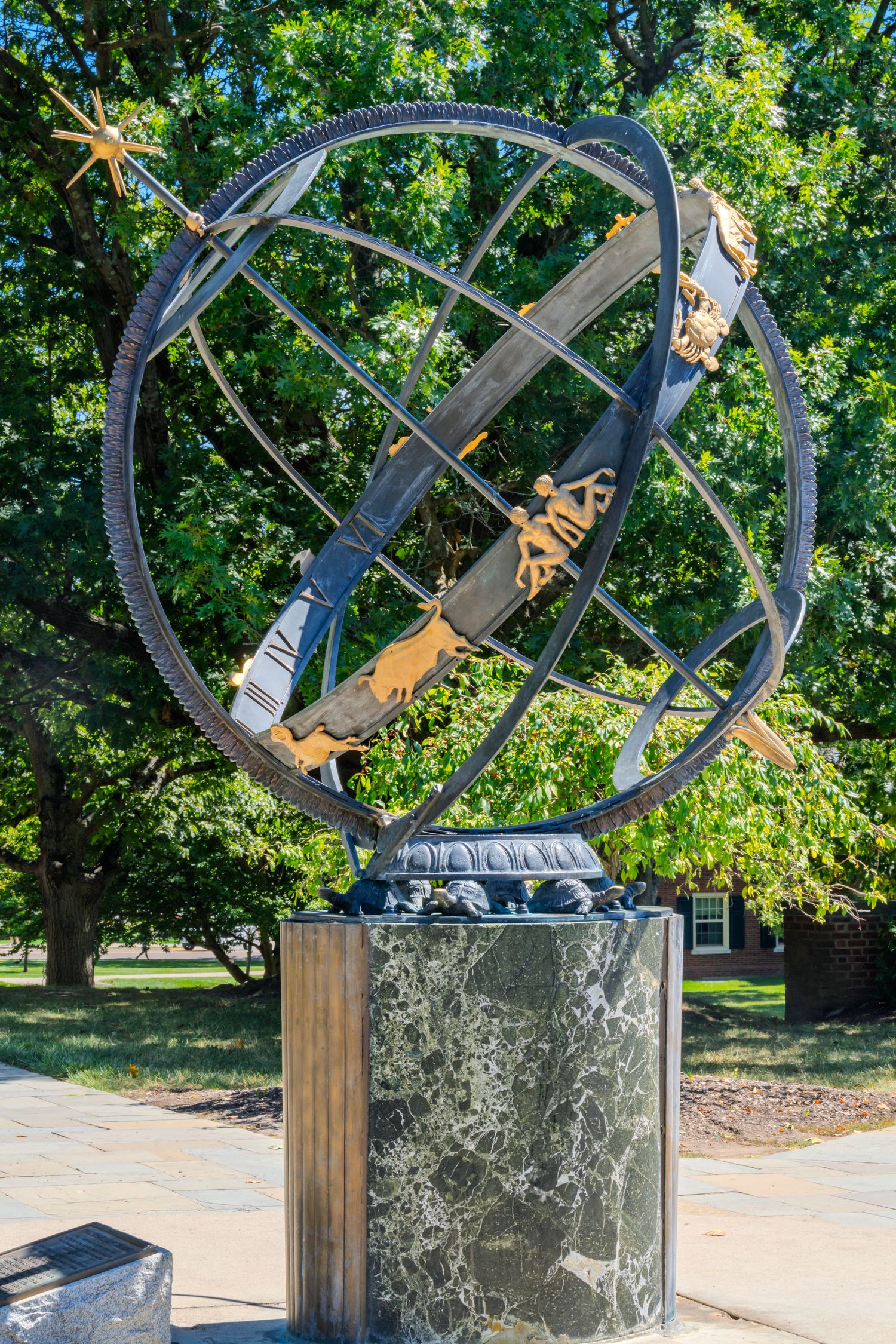 Large armillary sphere sculpture on marble pedestal surrounded by lush green trees in an outdoor garden setting.