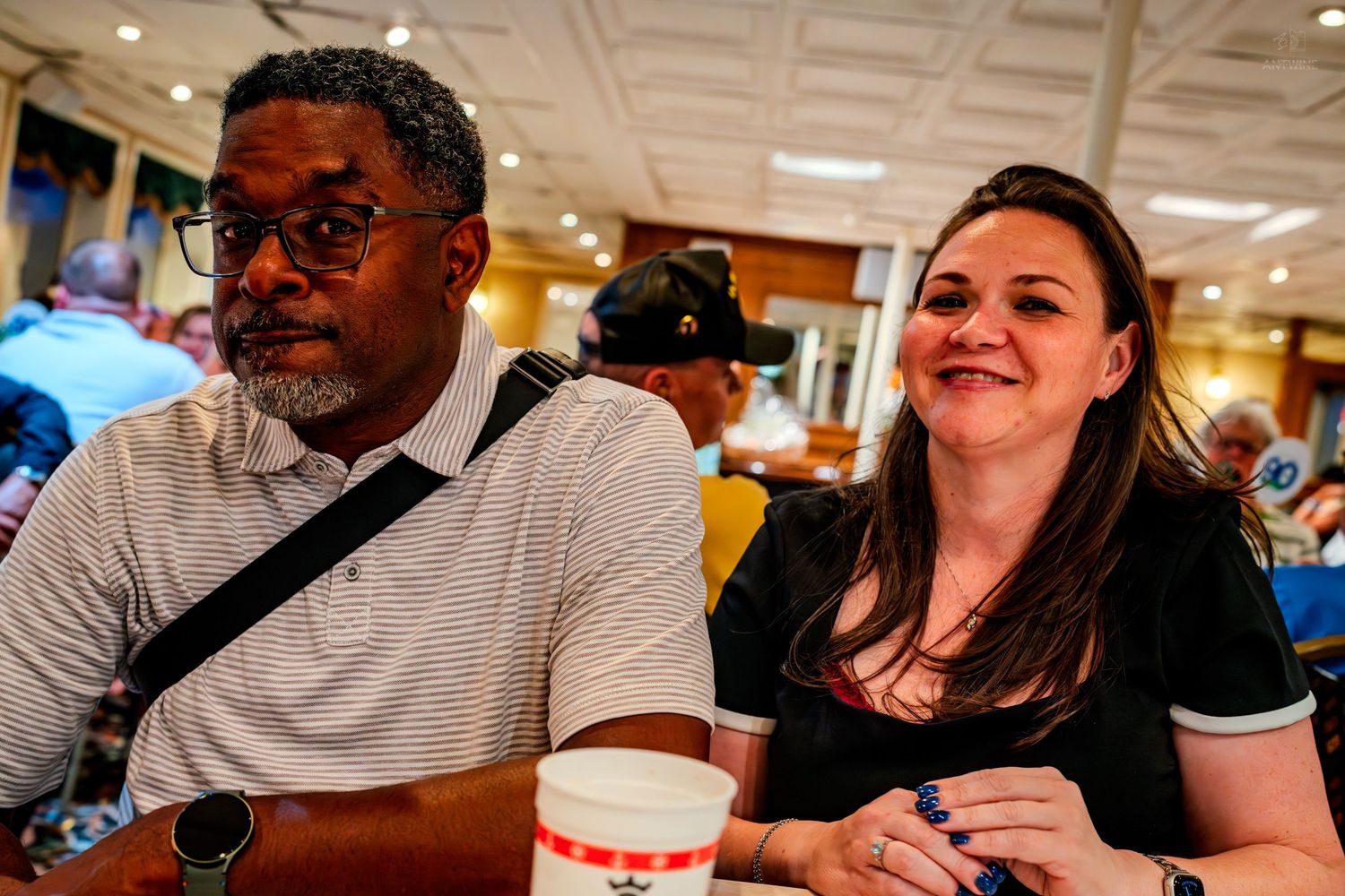 A man and woman smiling and chatting together at an indoor event with coffee cups on the table.
