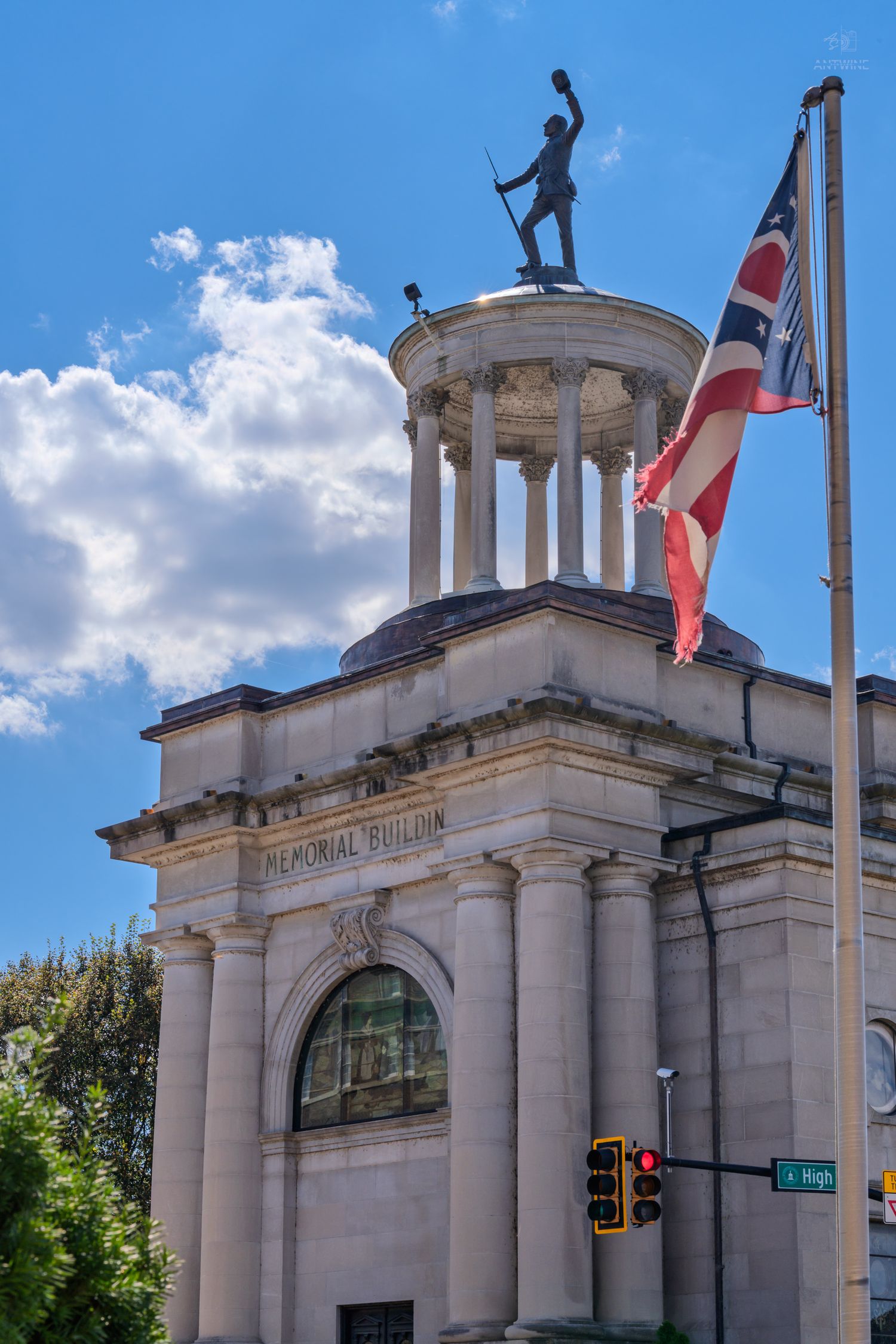 Historic Memorial Building with columned rotunda, soldier statue, and Ohio state flag against blue sky.
