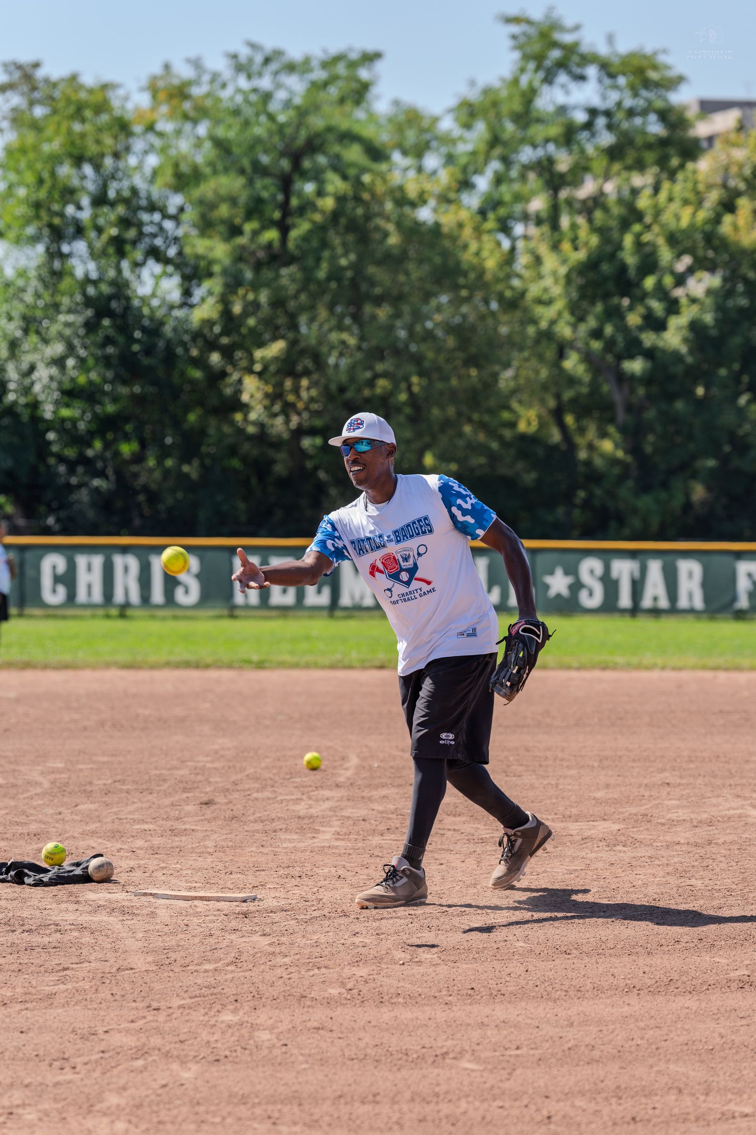 Athlete in white jersey throwing a softball on a sunny outdoor baseball field.