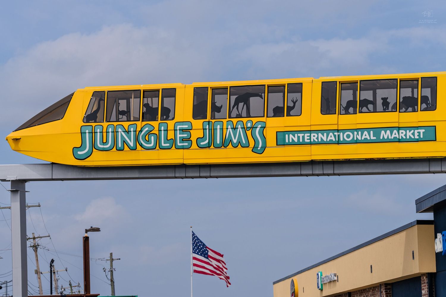 Jungle Jim's International Market yellow monorail train passing over a road with an American flag below.