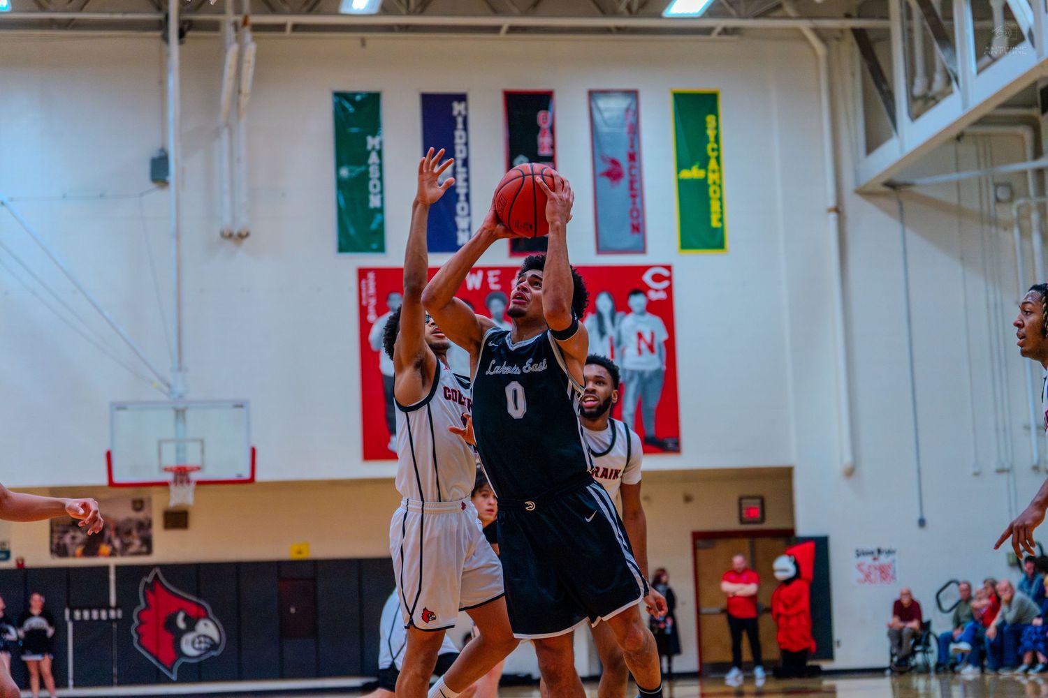 Player #0 attempts a jump shot over a defender during a high school basketball game indoors.
