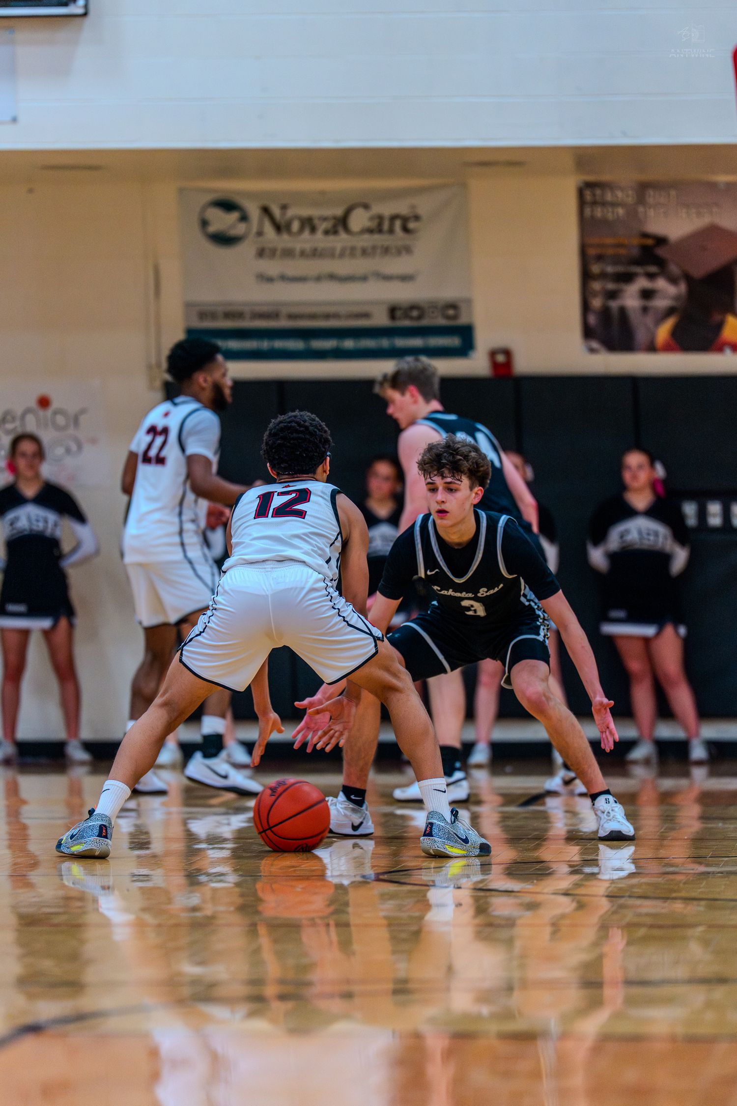 High school basketball player number 12 dribbles while being guarded during a game.