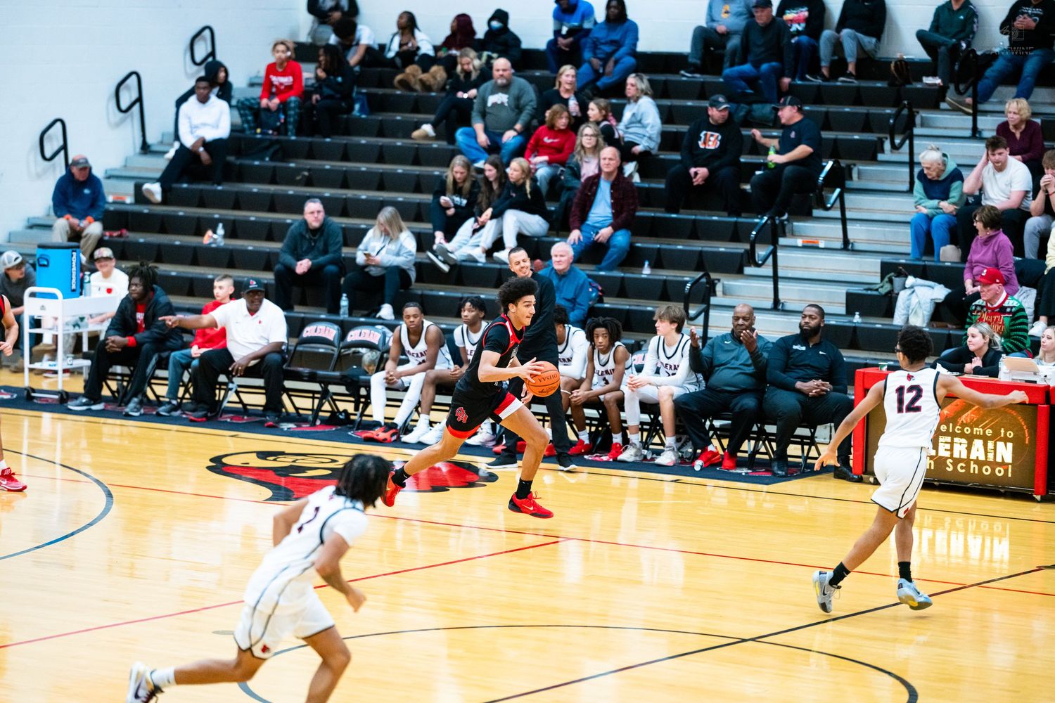 Basketball player drives toward basket as defenders react during high school game with crowd.