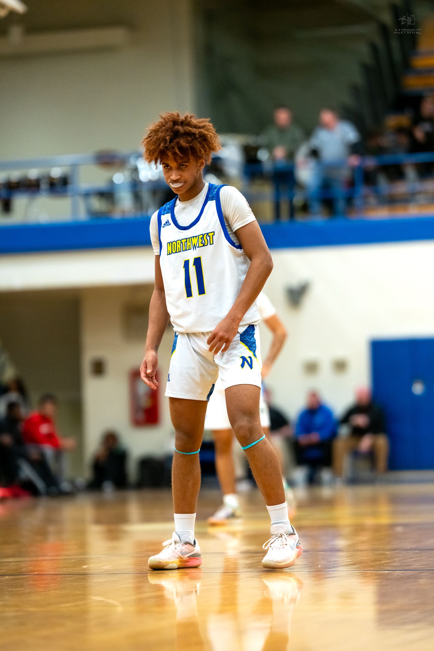 High school basketball player number 11 in Northwest uniform stands focused on court during game.
