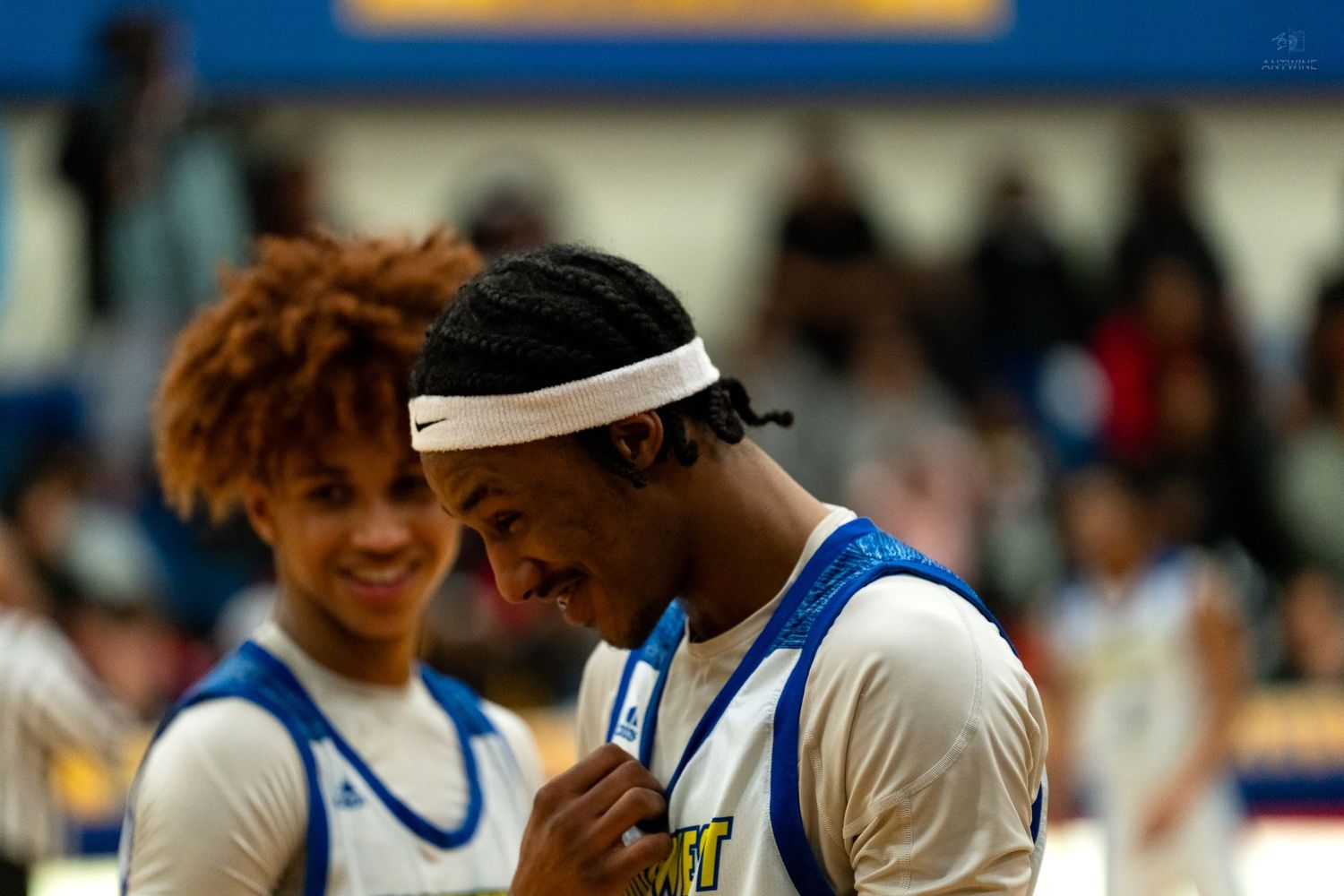 Two high school basketball players in blue uniforms share a moment on the sideline during a game.