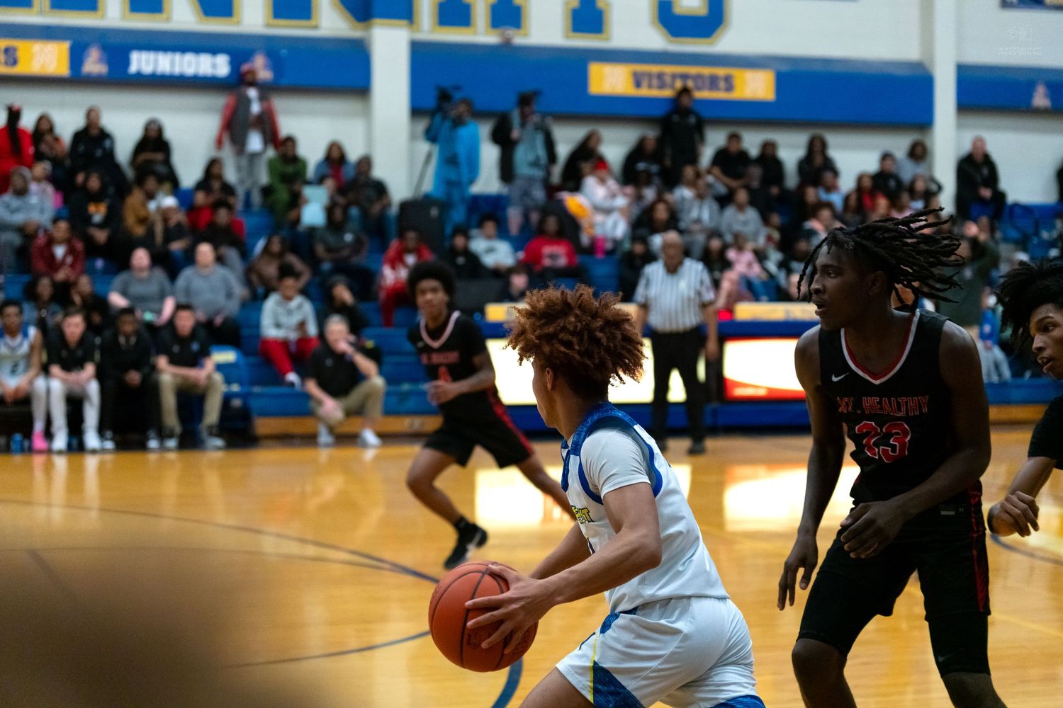 A high school basketball player dribbles past defenders during a competitive game in a packed gymnasium.