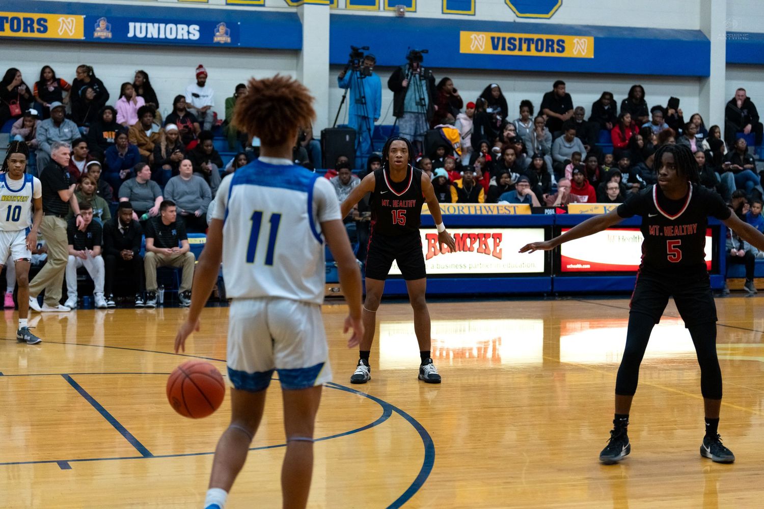 Basketball player number 11 in blue dribbles while two opponents in red defend during a game.