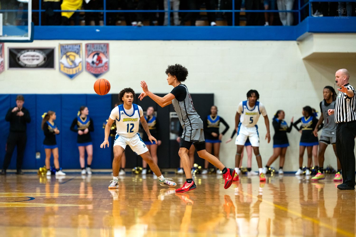 Basketball player #12 guards opponent as teammates watch from sideline.