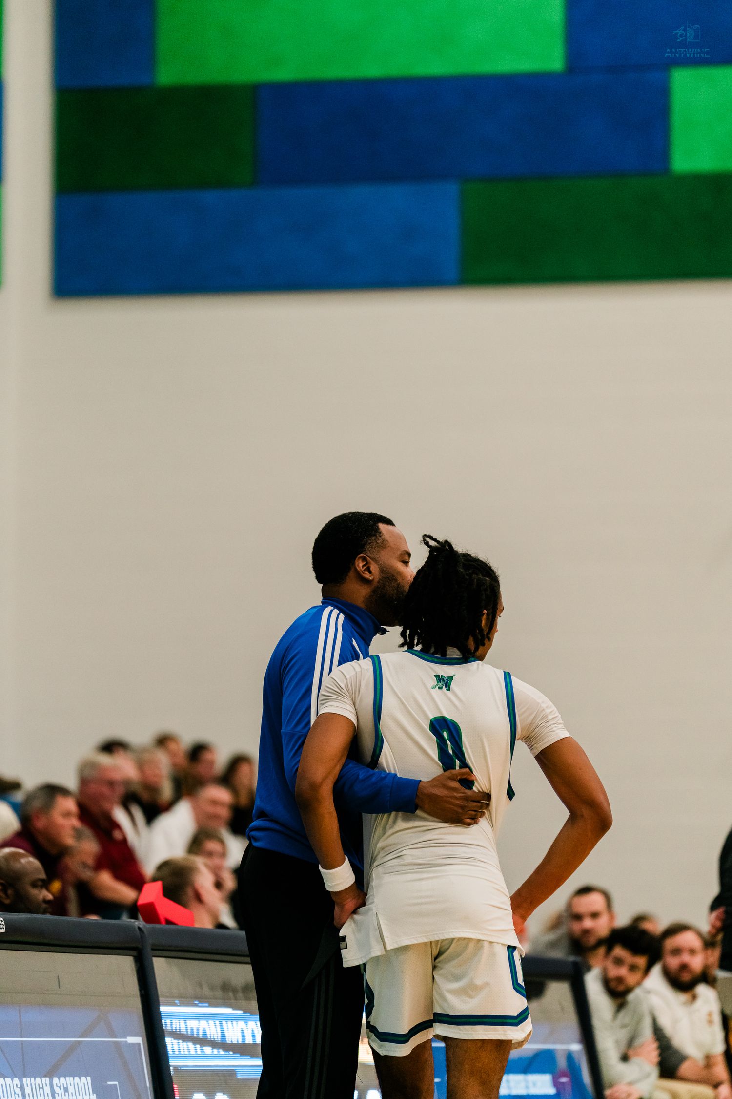 Coach whispers strategy to Warriors player number 0 on the sideline during a basketball game.