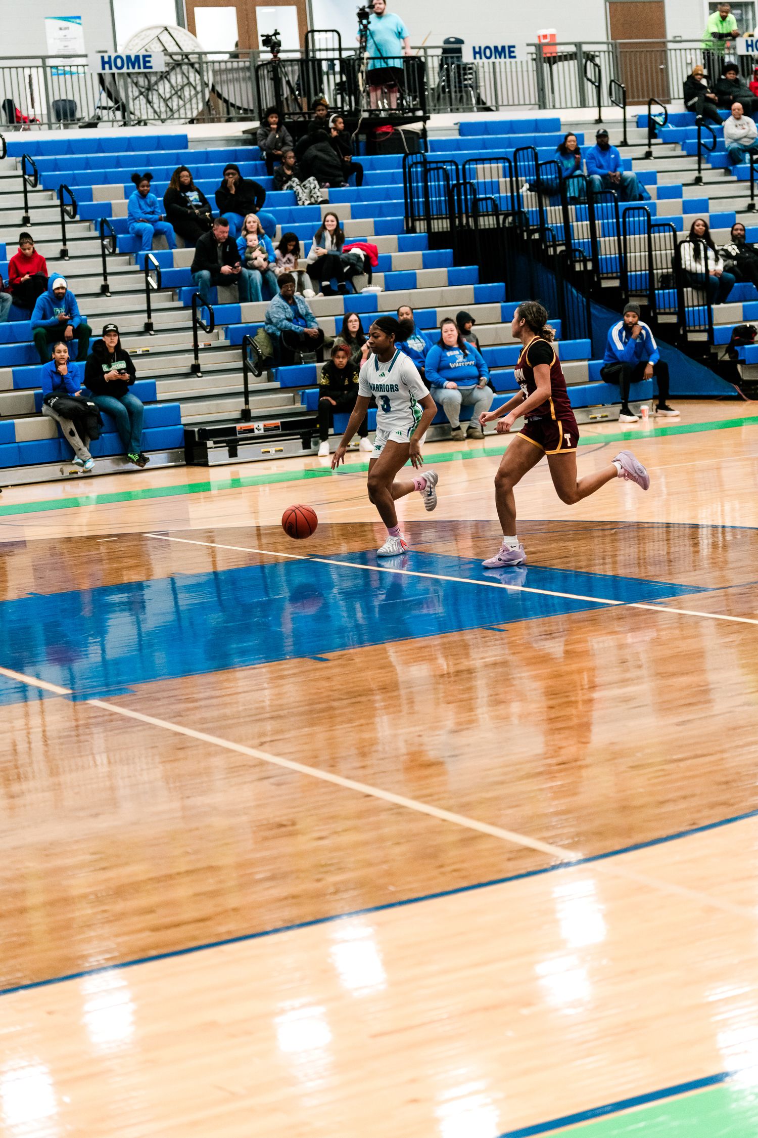 Girls basketball player in white dribbles past maroon-uniformed defender on hardwood court.