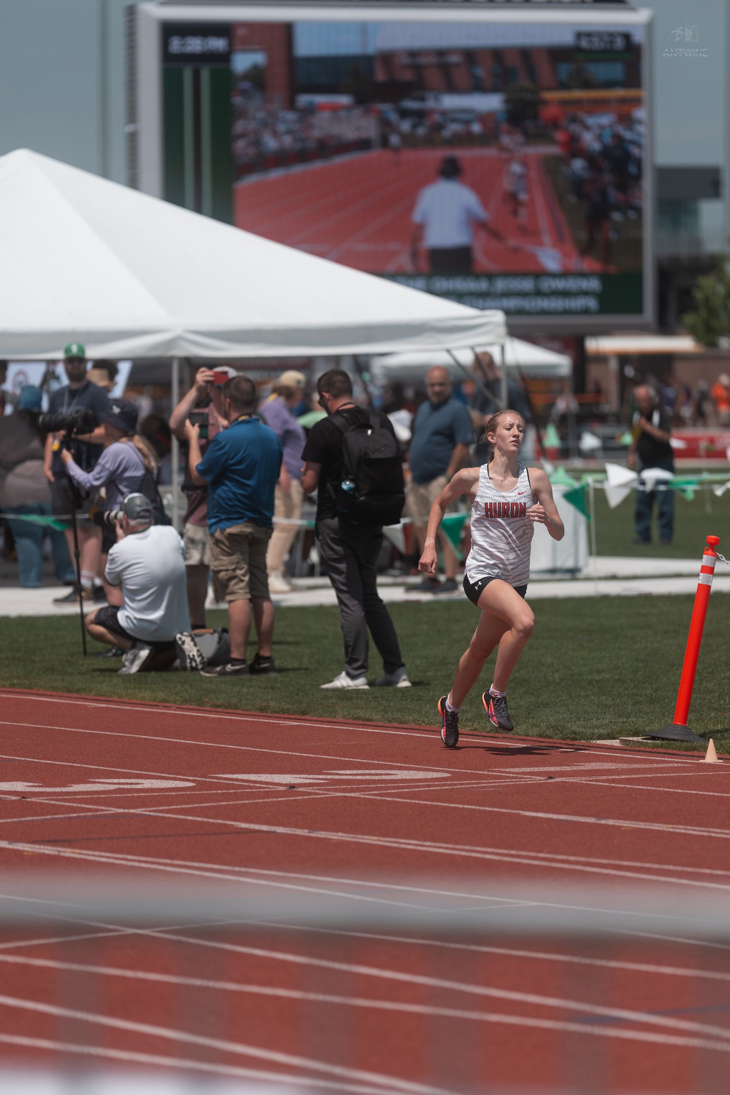 Female runner in white Mariners uniform competes on a red track at Jesse Owens Memorial Stadium championship meet.