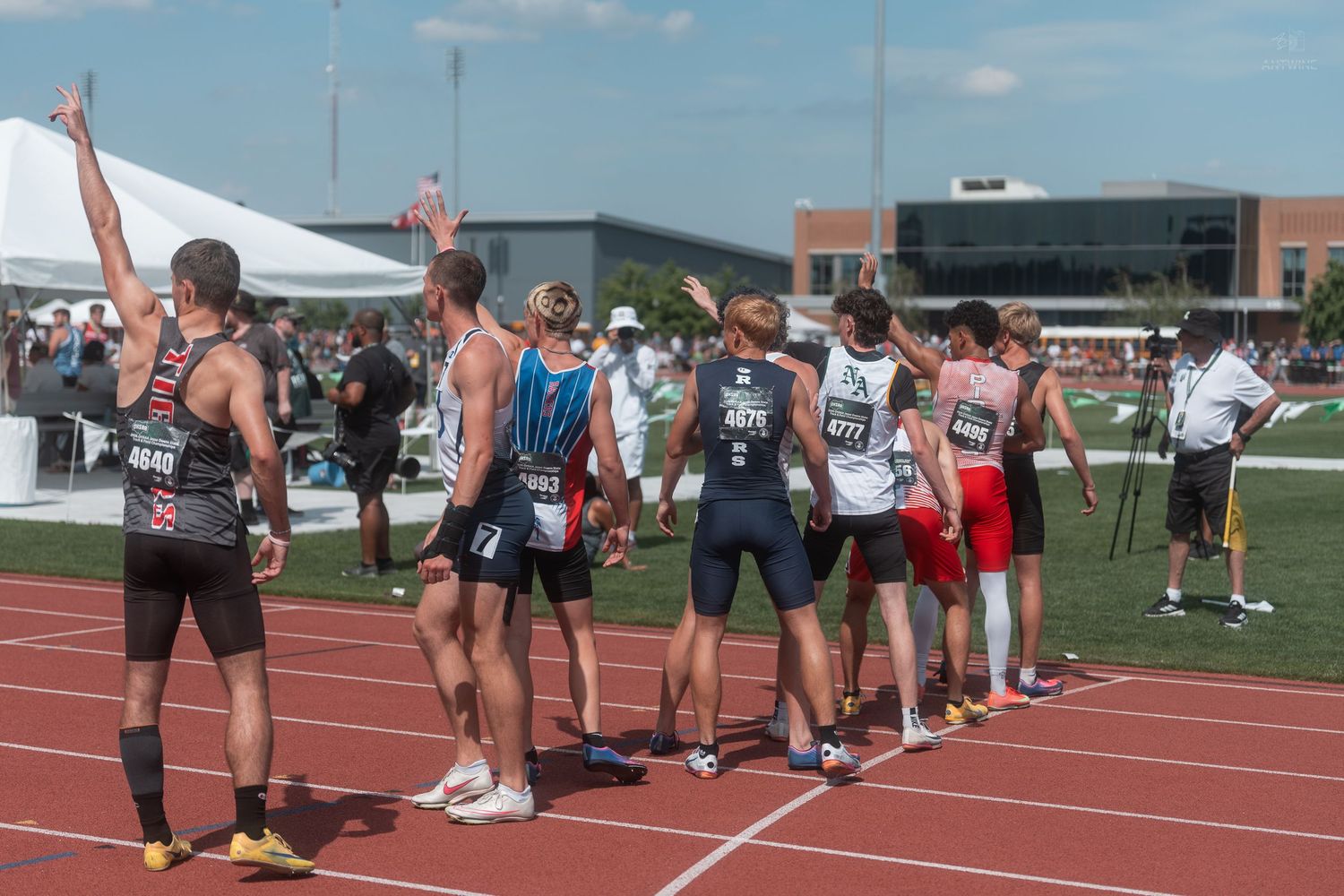Track athletes raise hands in celebration while gathered on red track after relay race at championship.
