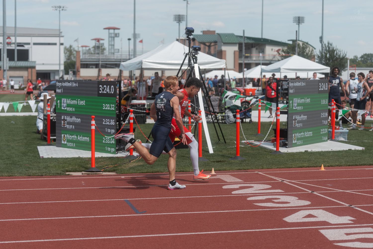 Athlete crosses finish line at outdoor track and field championship event with results board visible nearby.
