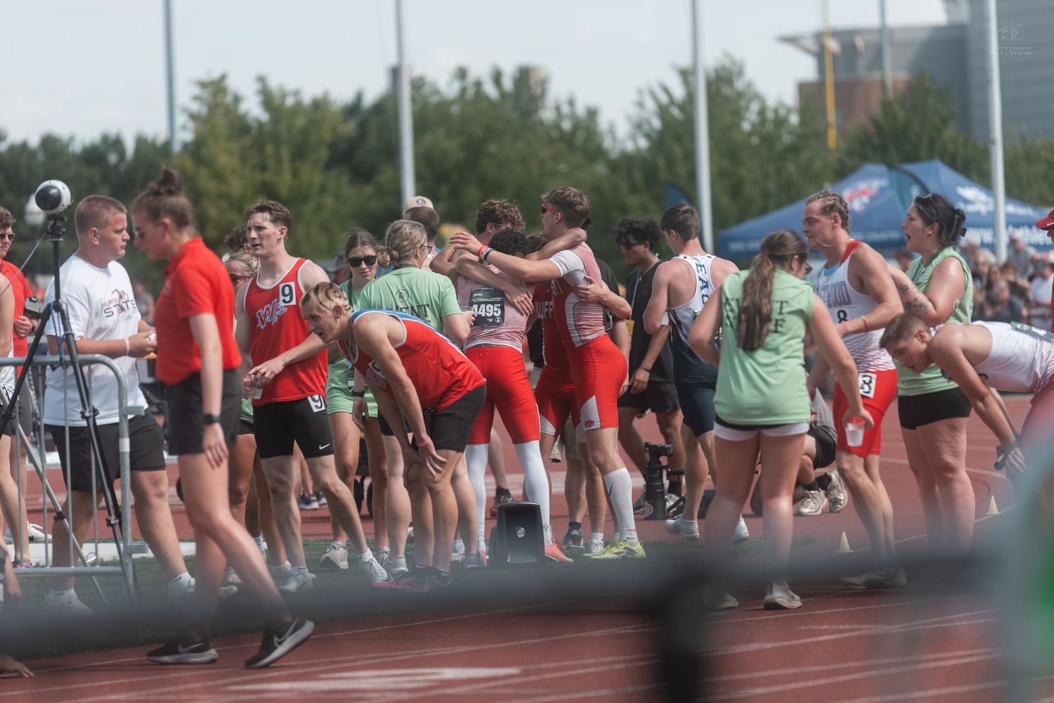 Athletes in red and green uniforms embrace and celebrate on a red track after a race.