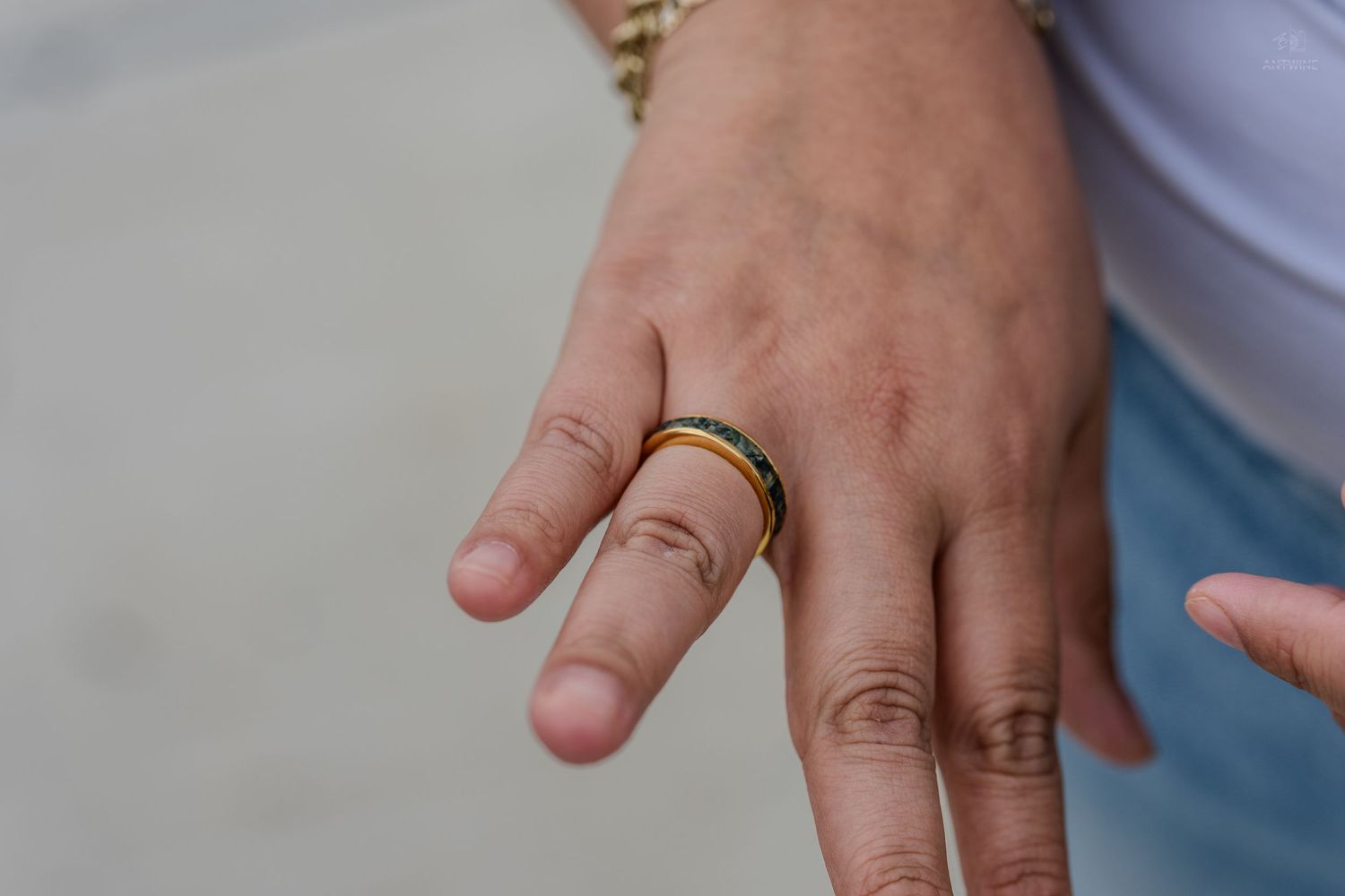 Close-up of a hand wearing a colorful blue and yellow band ring with a gold bracelet.