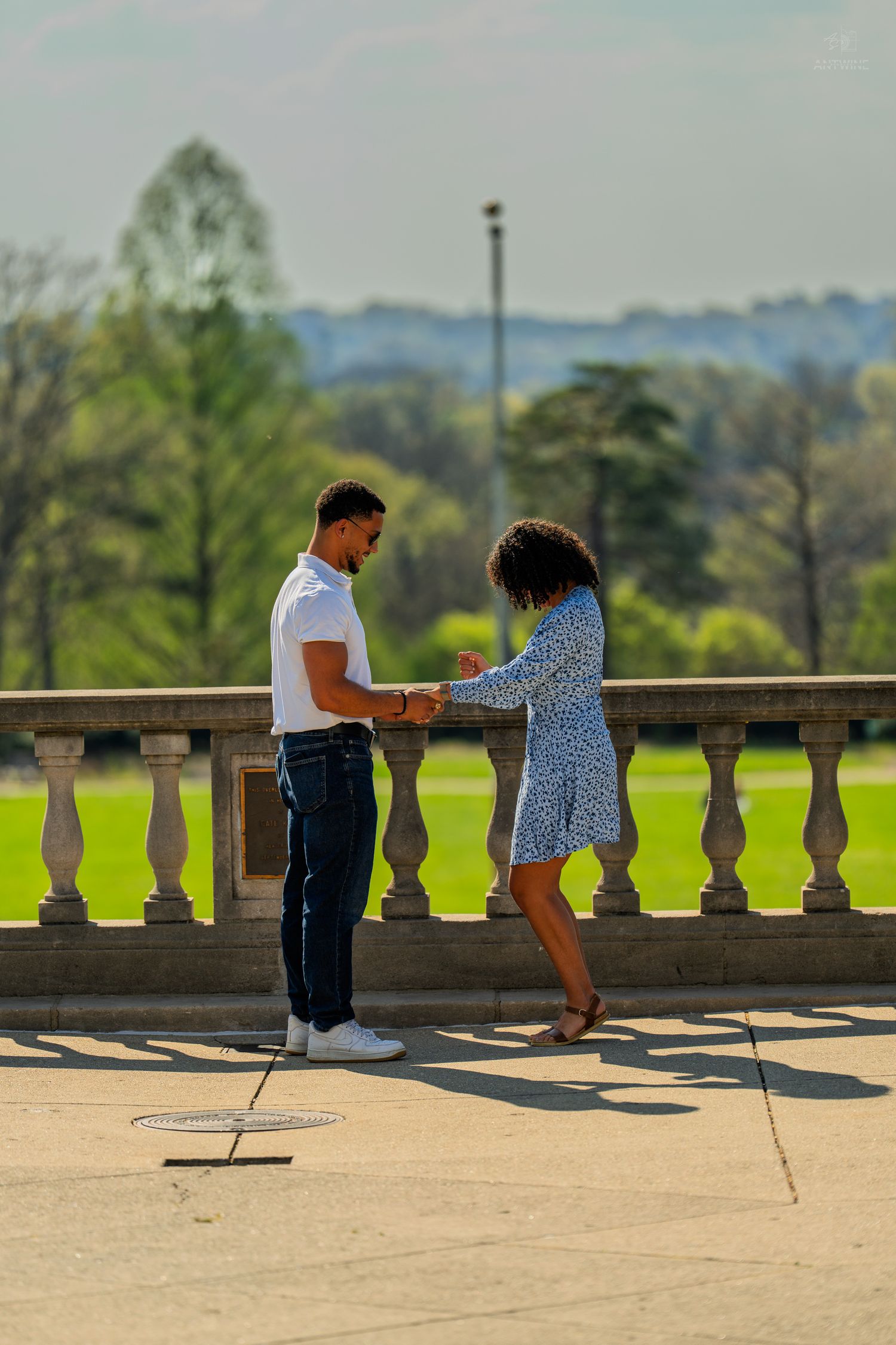 Couple joyfully holding hands on a sunlit stone balcony terrace surrounded by spring greenery.
