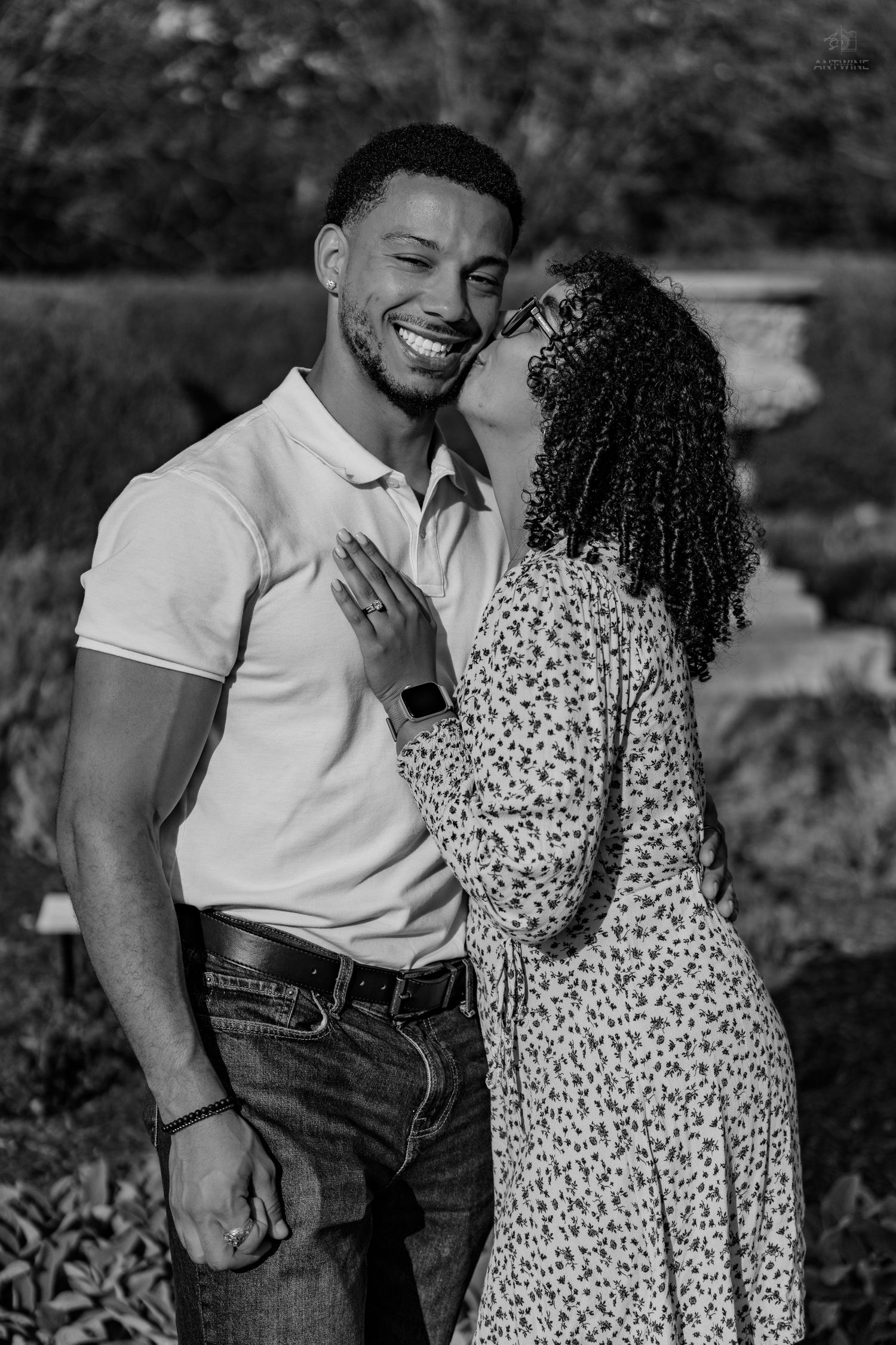 Black and white photo of a joyful couple embracing, woman kissing mans cheek as he smiles broadly.