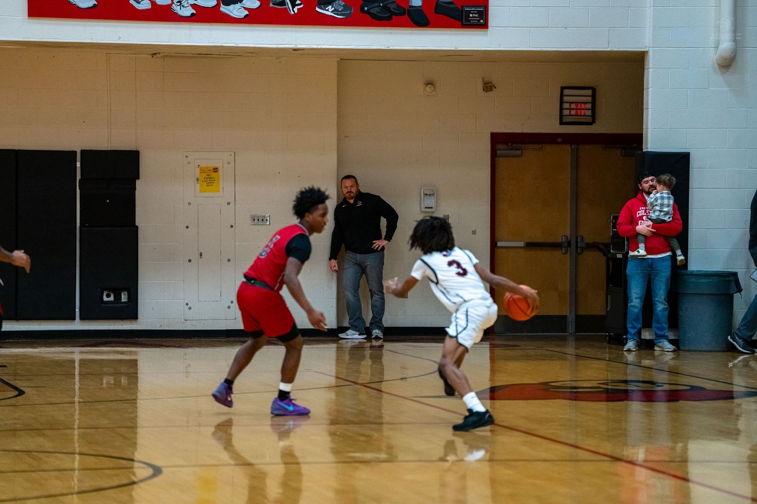 Two high school basketball players face off on court as referee watches during indoor gymnasium game.
