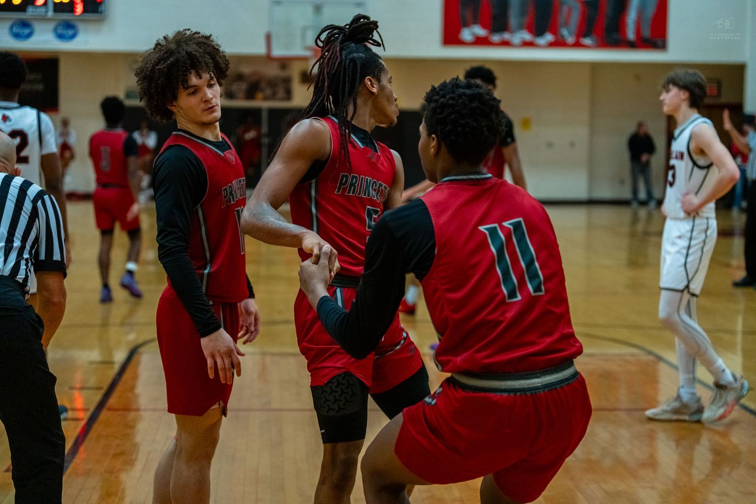 Three high school basketball players in red uniforms huddle together during a game timeout.