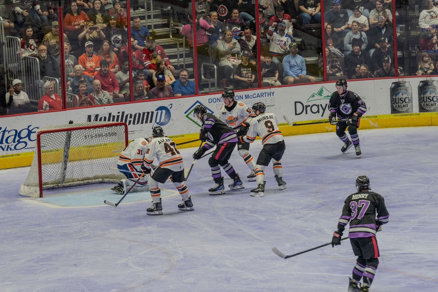 Ice hockey teams battle near the orange and white goal as player number 37 skates nearby.