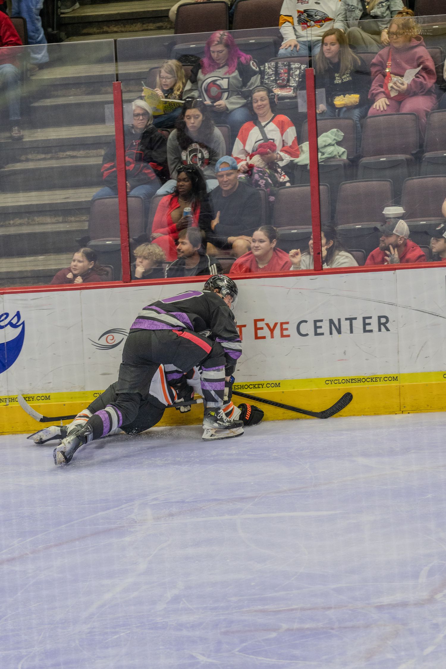 Ice hockey player checks opponent against the boards near the Eye Center advertisement.