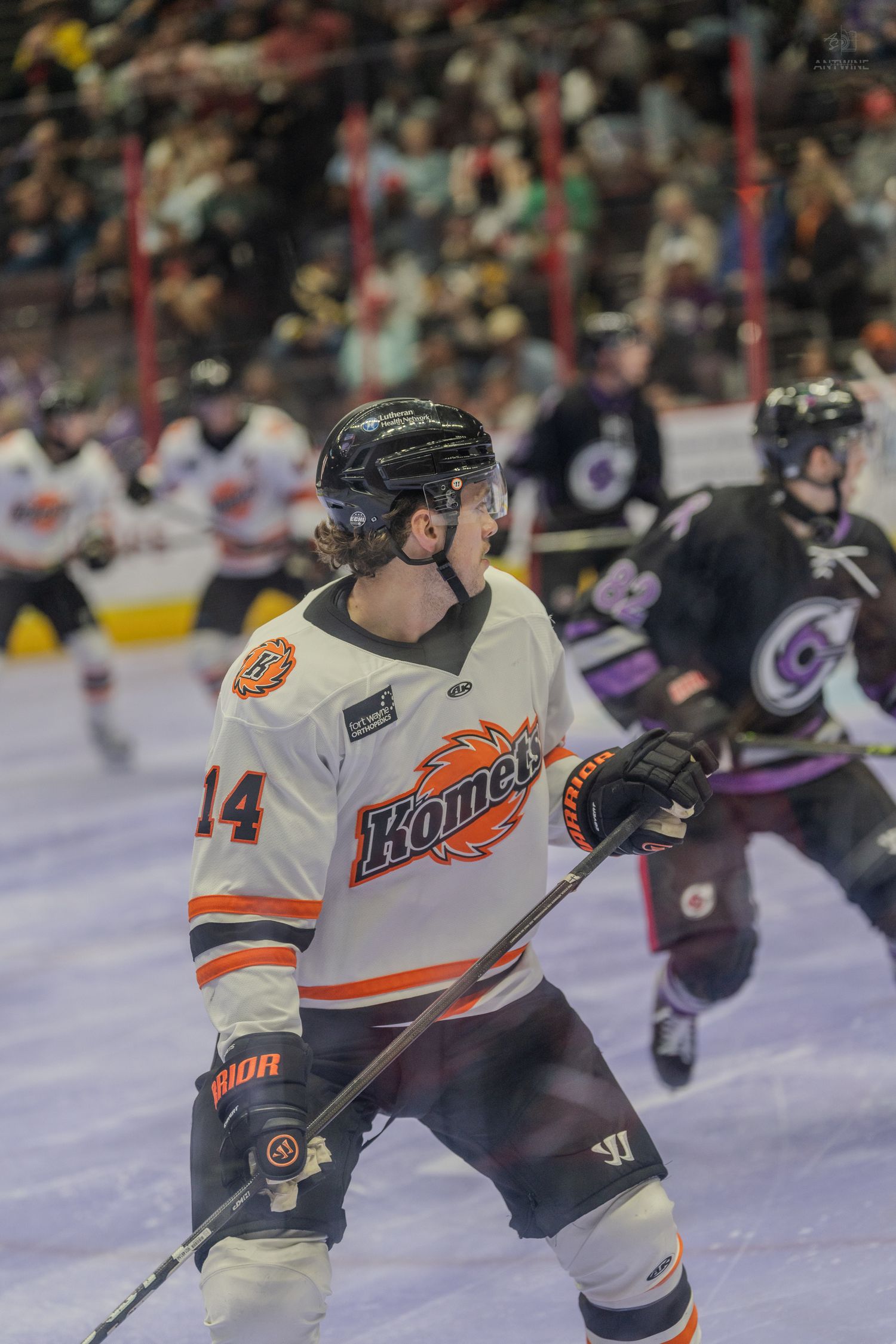 Fort Wayne Komets #14 in white and orange jersey skating on ice during a competitive hockey match.