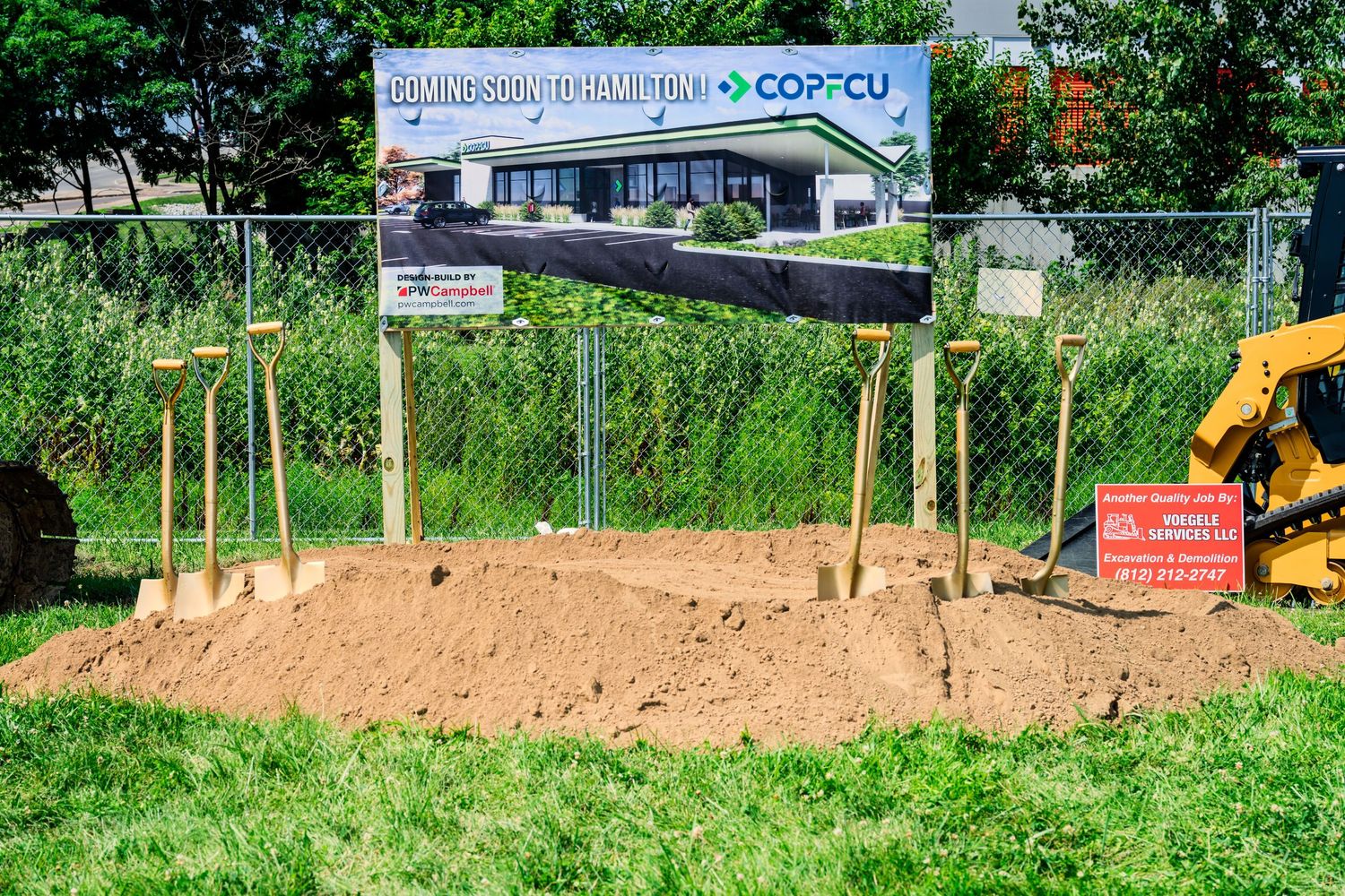 COPCU credit union groundbreaking site with golden shovels in dirt mound and coming soon banner in Hamilton.