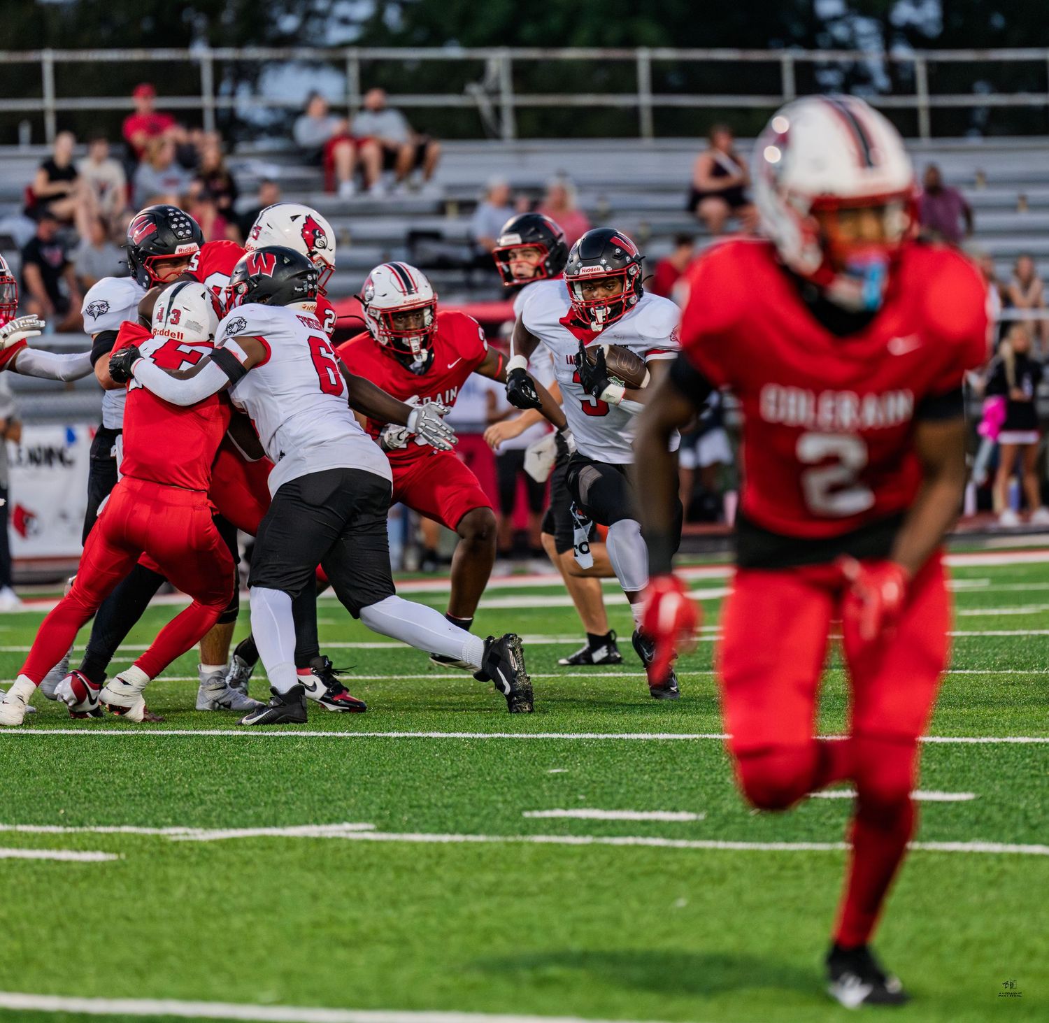 Colerain football players in red uniforms defend against an opponent run during a high school football game.
