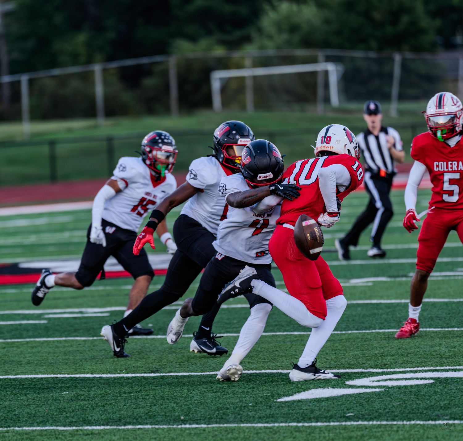 A red-uniformed quarterback scrambles away from defenders during a high school football game.