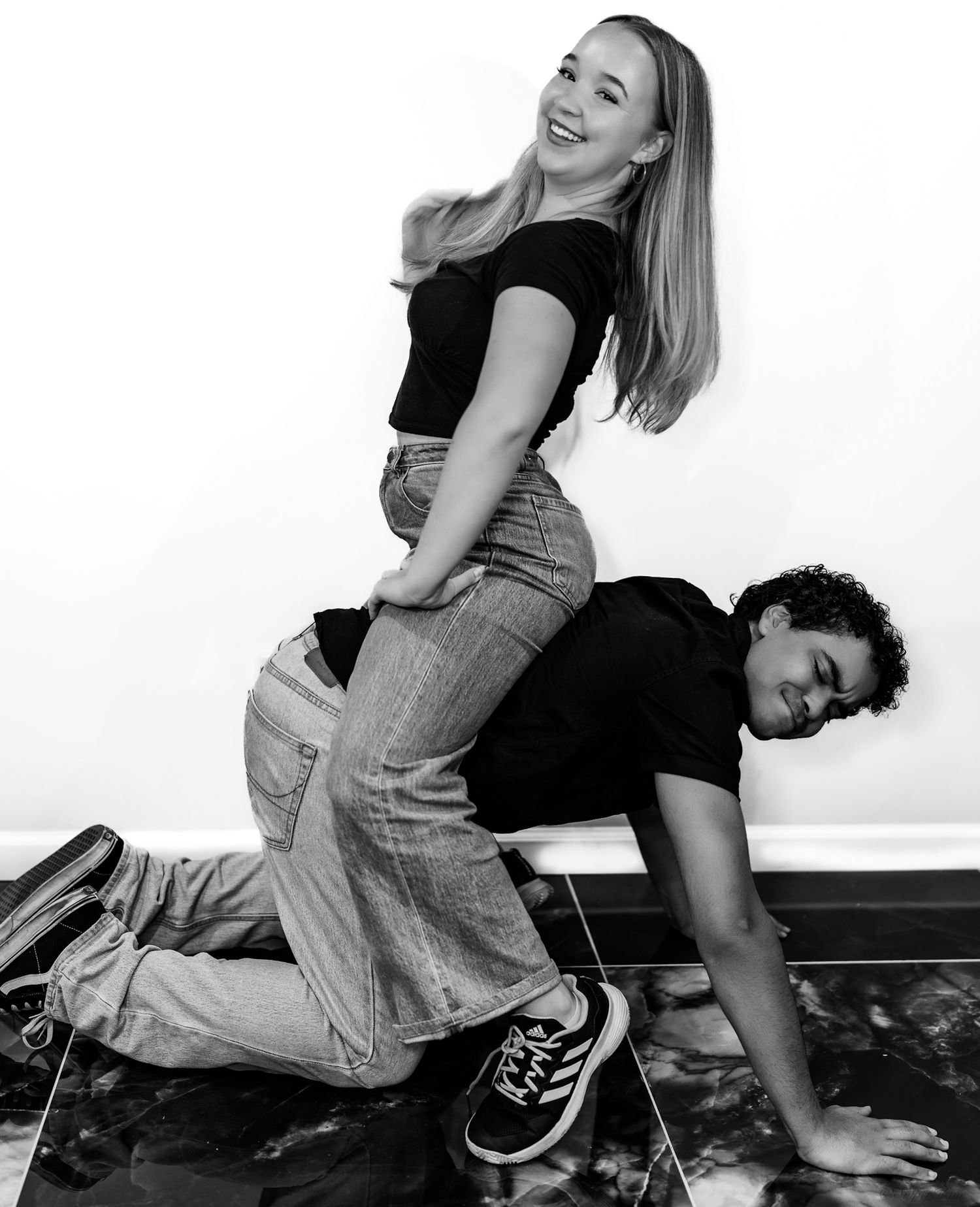 Two young dancers posing playfully in black and white, girl standing on boy's back.