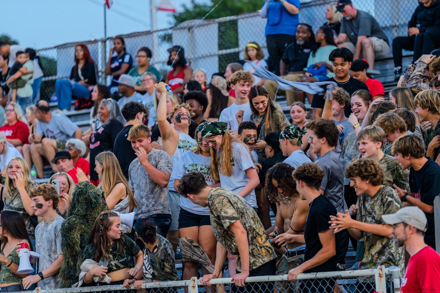 Enthusiastic high school football fans cheer in the bleachers during a Friday night game.