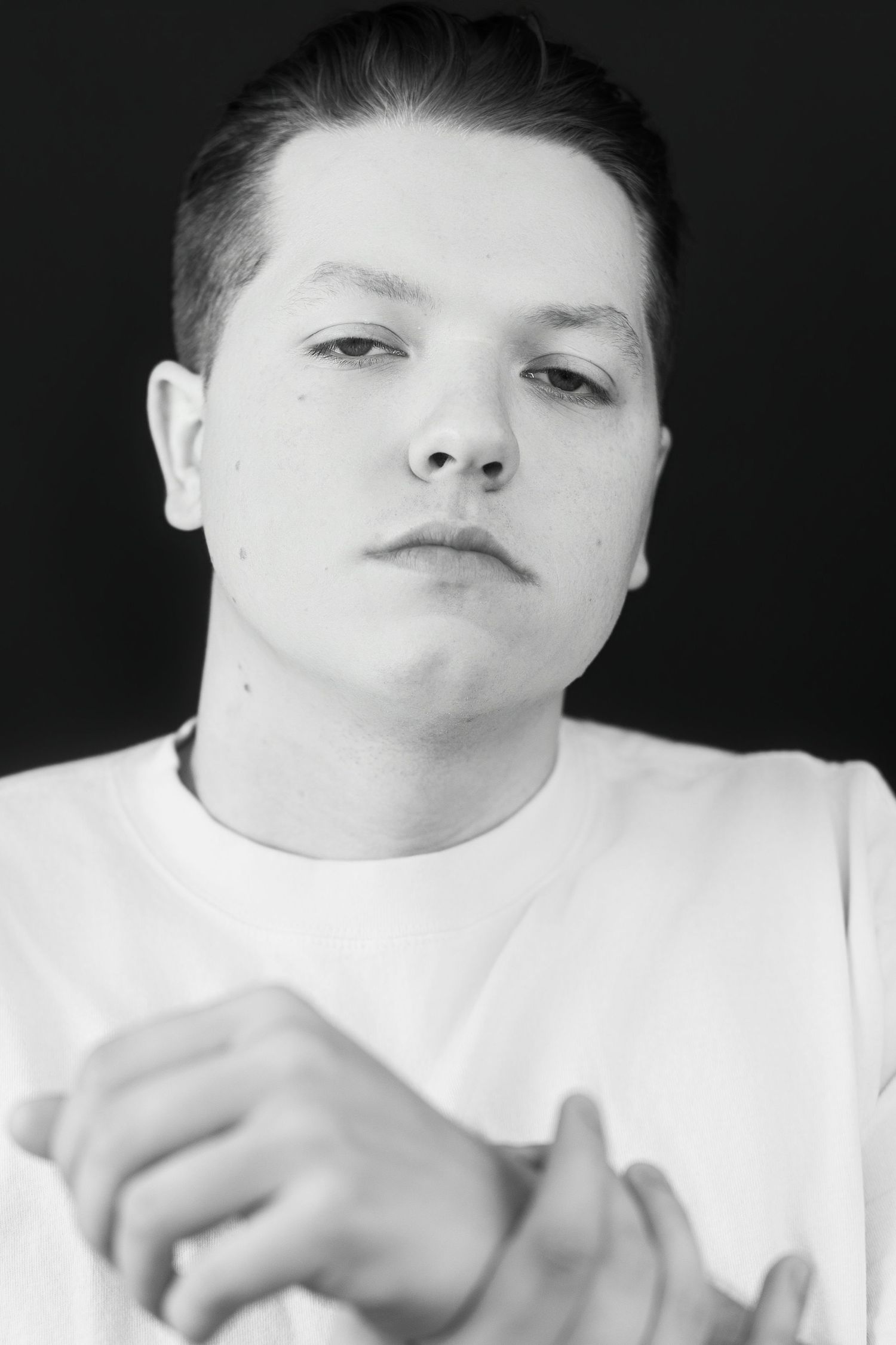 Black and white portrait of young man in white t-shirt clasping hands, serious look.