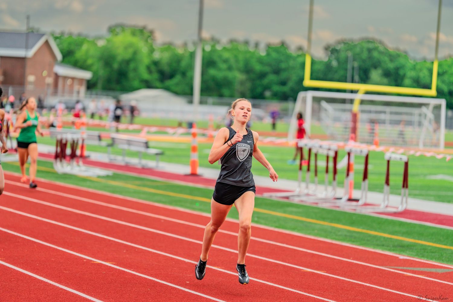 Female athlete in black sprints toward finish line at outdoor track meet.