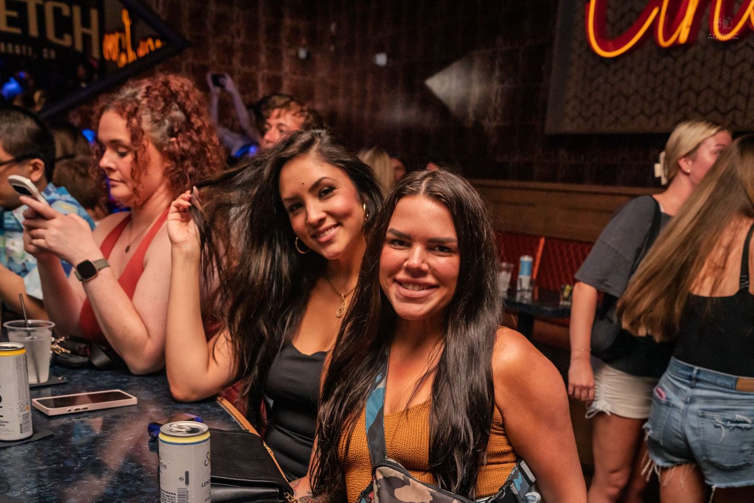 Three women smiling and posing together at a vibrant nightclub bar.