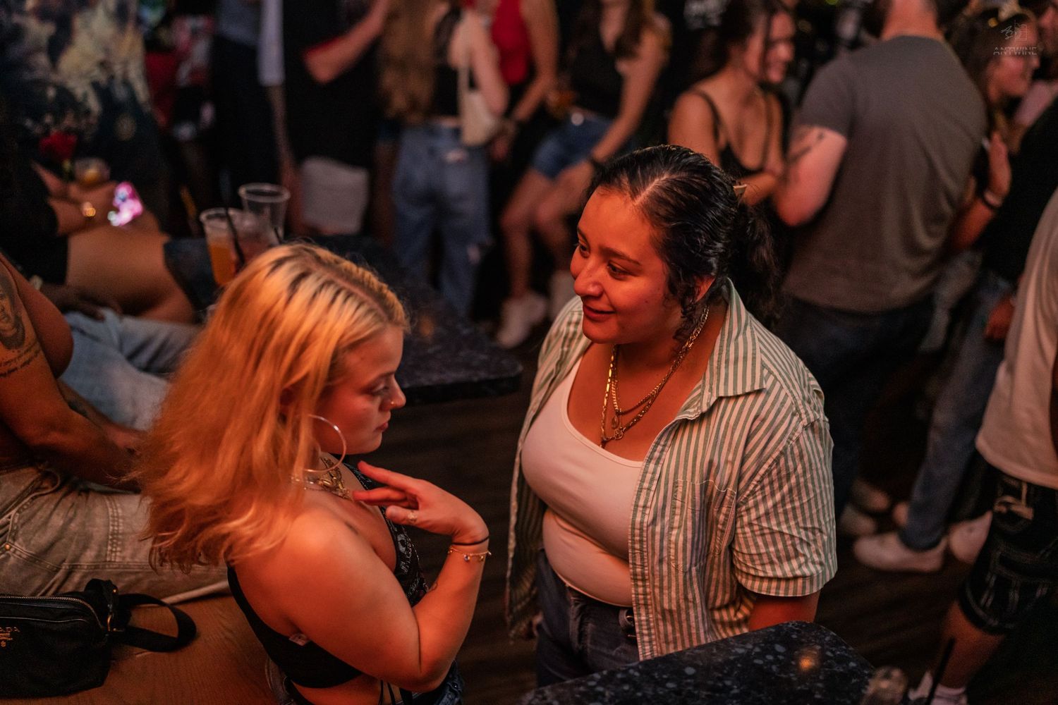 Two young women talking closely together at a lively nightclub party.