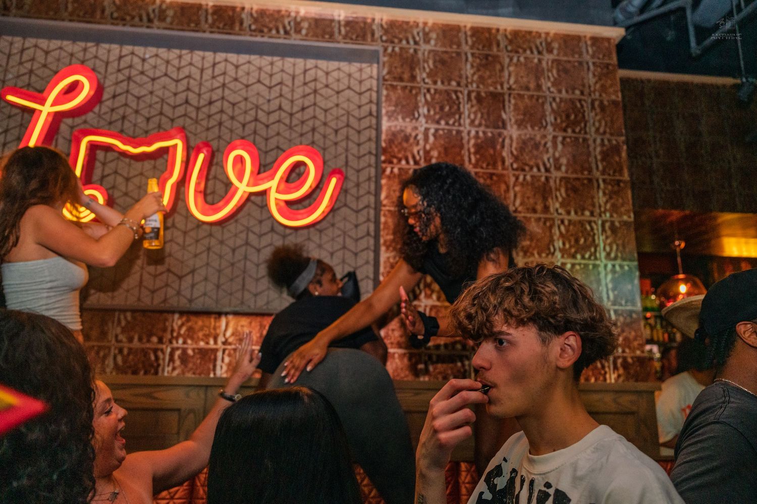 Young people socializing under a glowing Love neon sign at a Cincinnati bar.